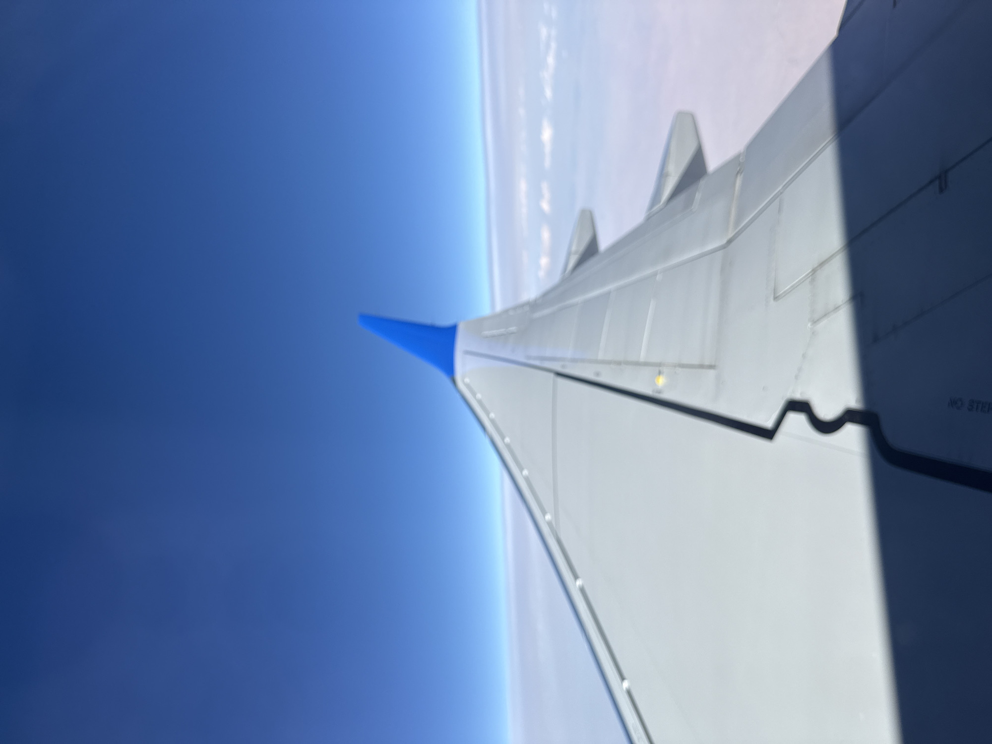 In-flight views: clouds, blue-tipped wing, and mountain ranges at dawn