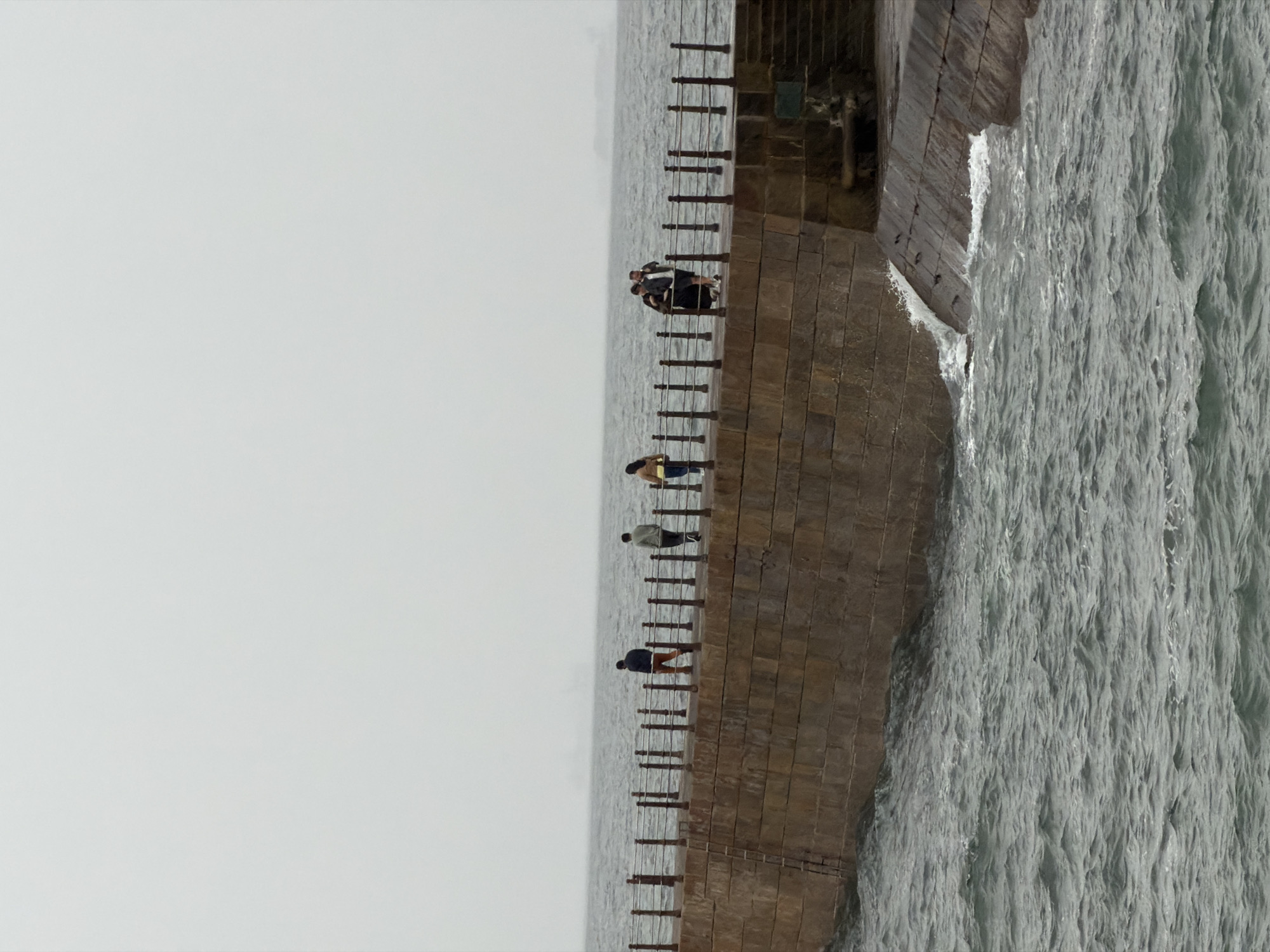 People gather on stone breakwater amid rough Atlantic seas