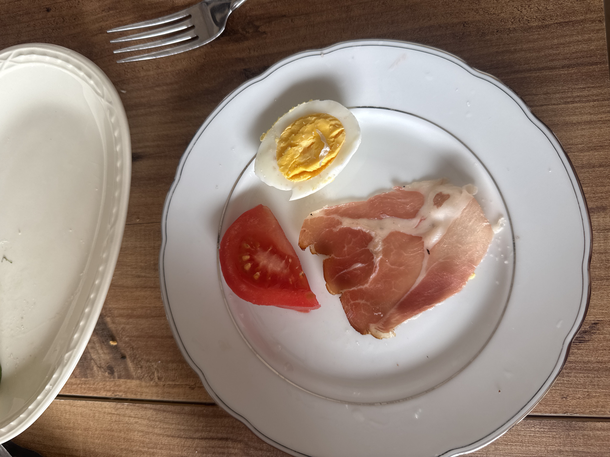 Morning meal documented featuring egg, tomato, prosciutto on wooden table