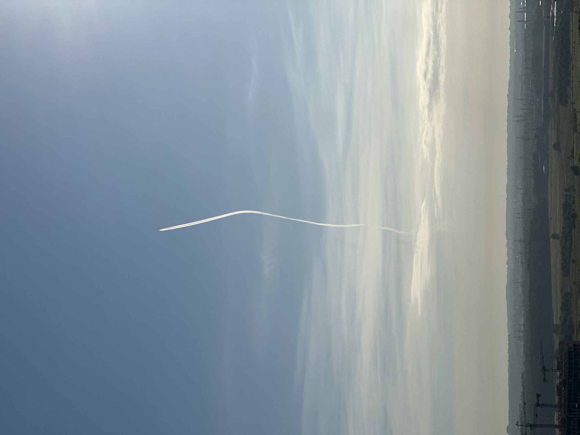 Contrail curves across a blue sky over Otradnoye
