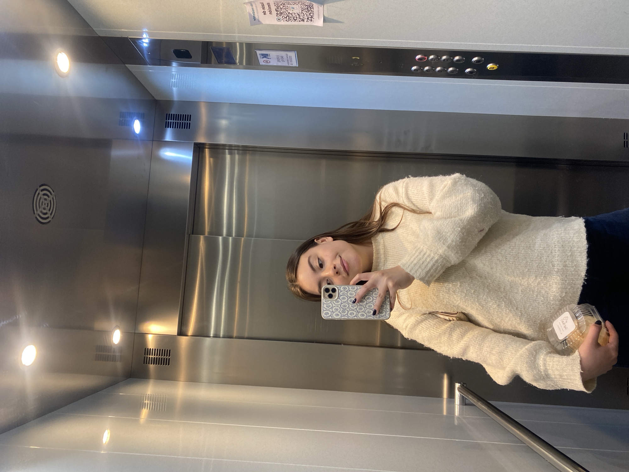 Woman Takes Elevator Selfie While Holding Cinnamon Roll Container