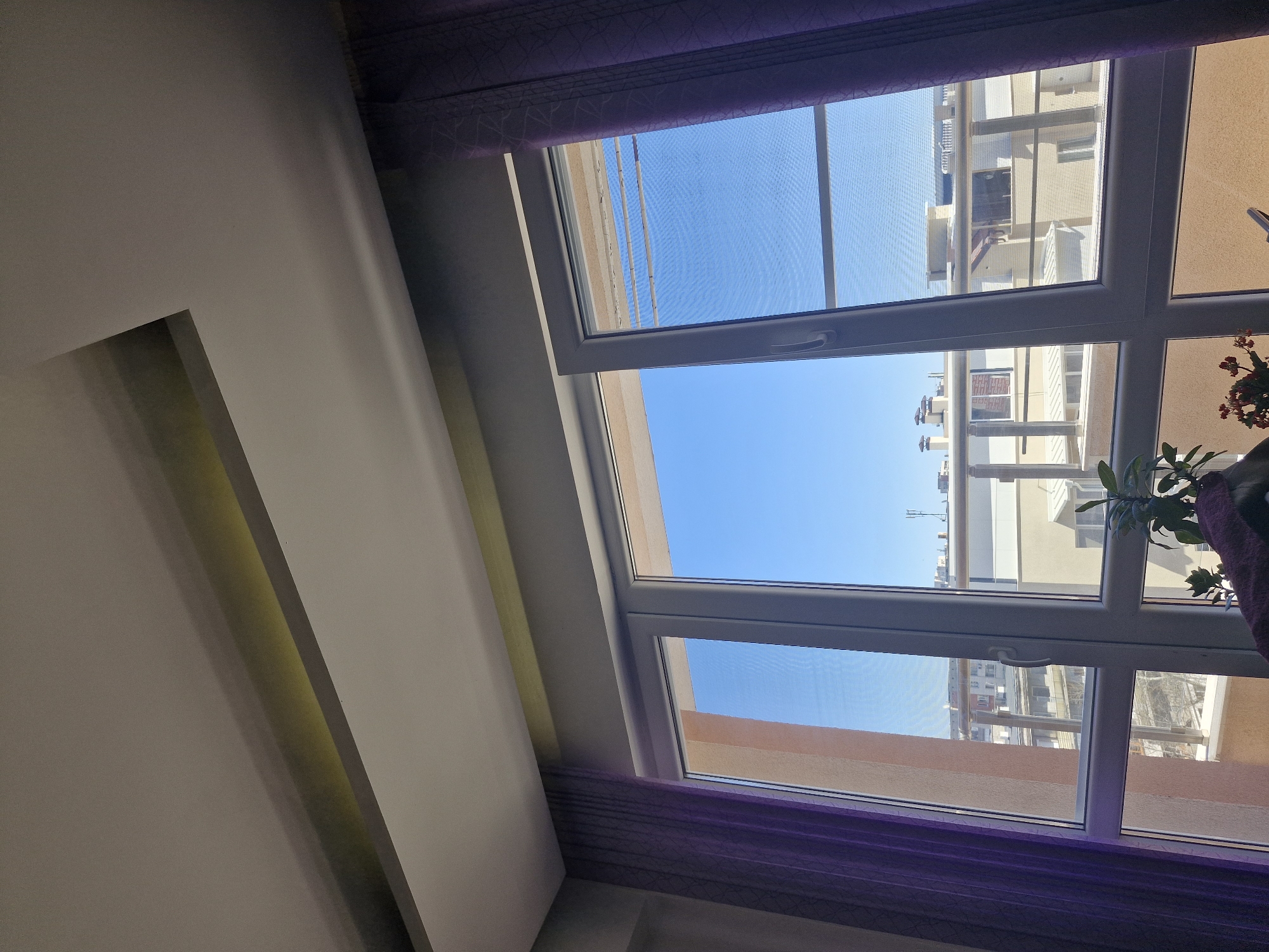 City view captured through violet-curtained window on clear day