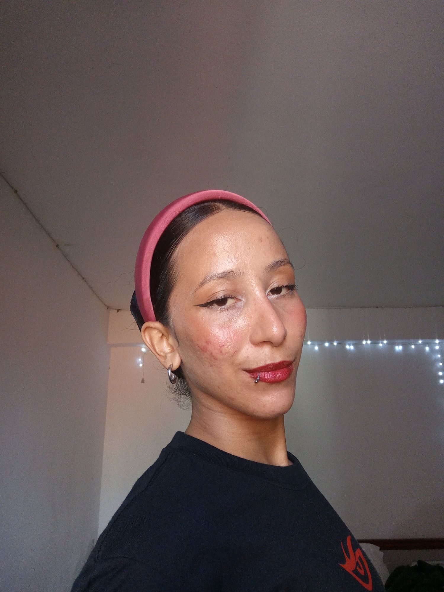 Person takes selfies indoors wearing pink headband, piercings visible