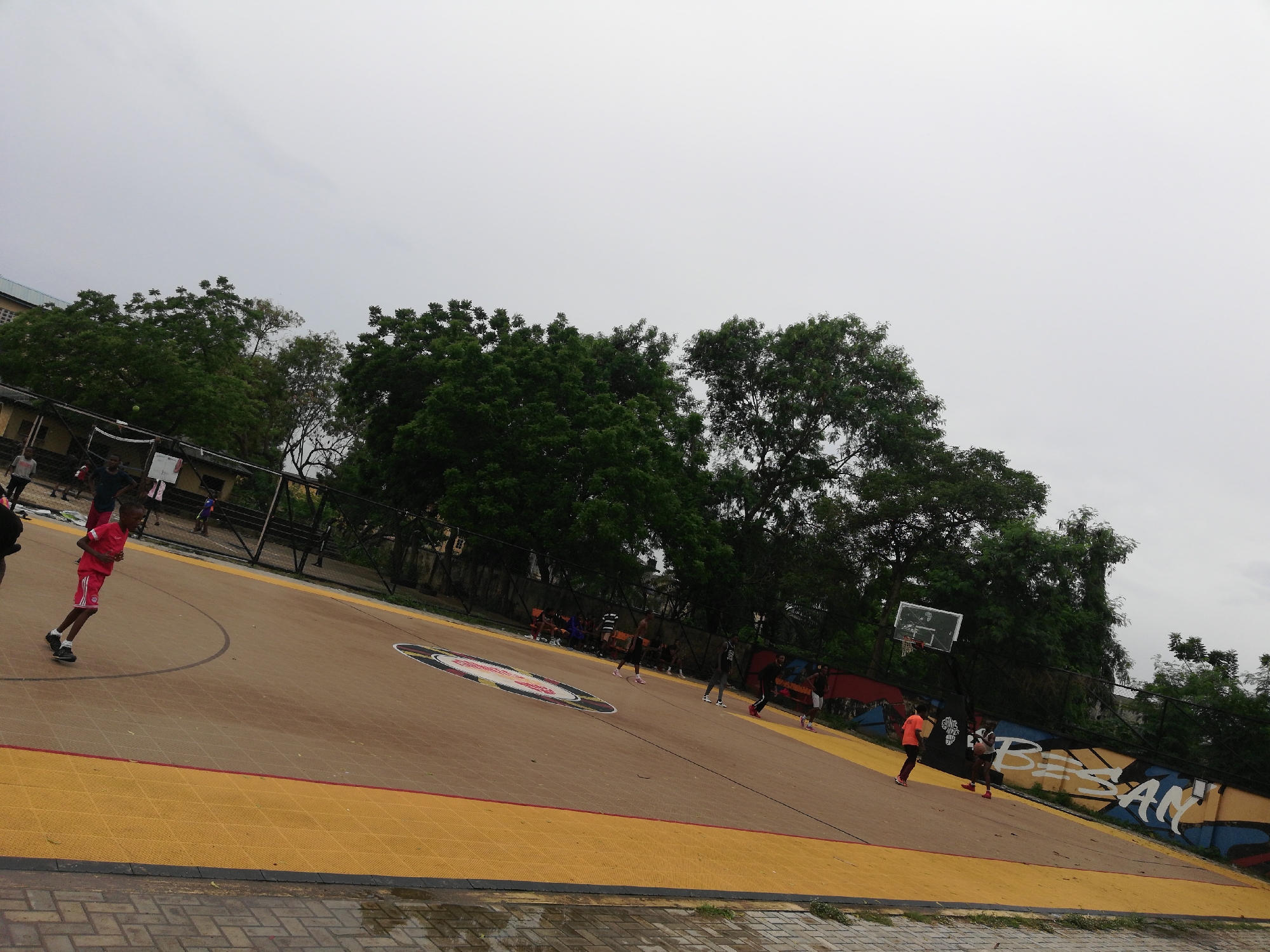 Young people play basketball at Lagos court during overcast afternoon