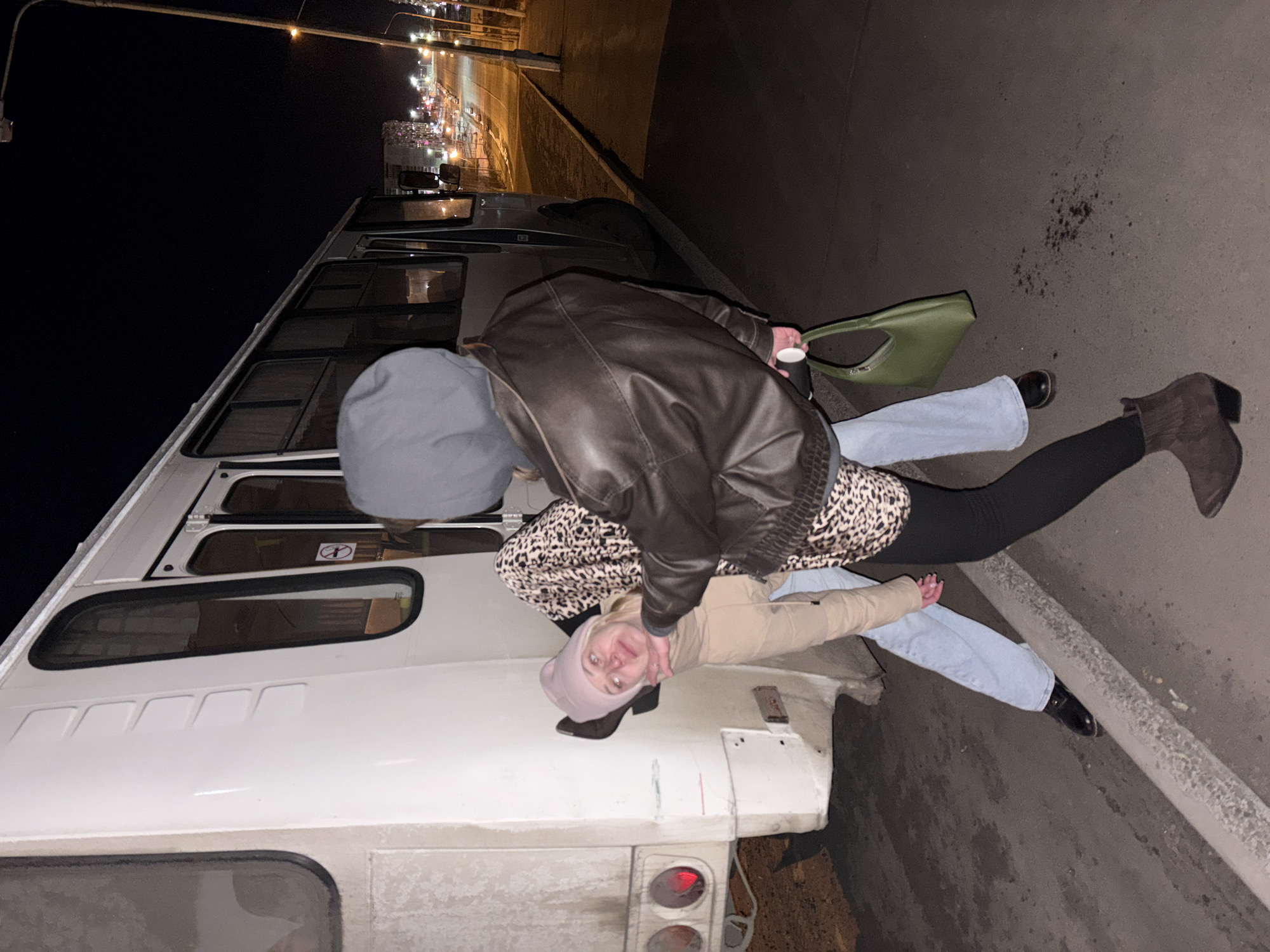 Two people interact near white vehicle in Ust-Ilimsk nighttime