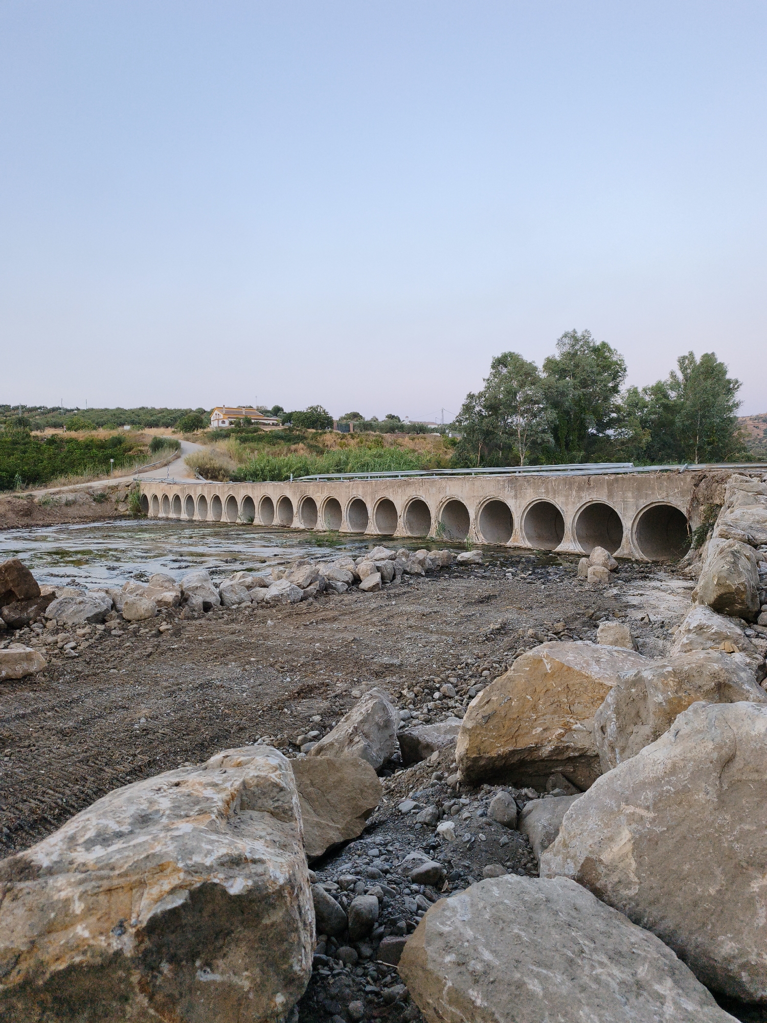 Arched bridge crosses rocky riverbed through rural Andalusian countryside