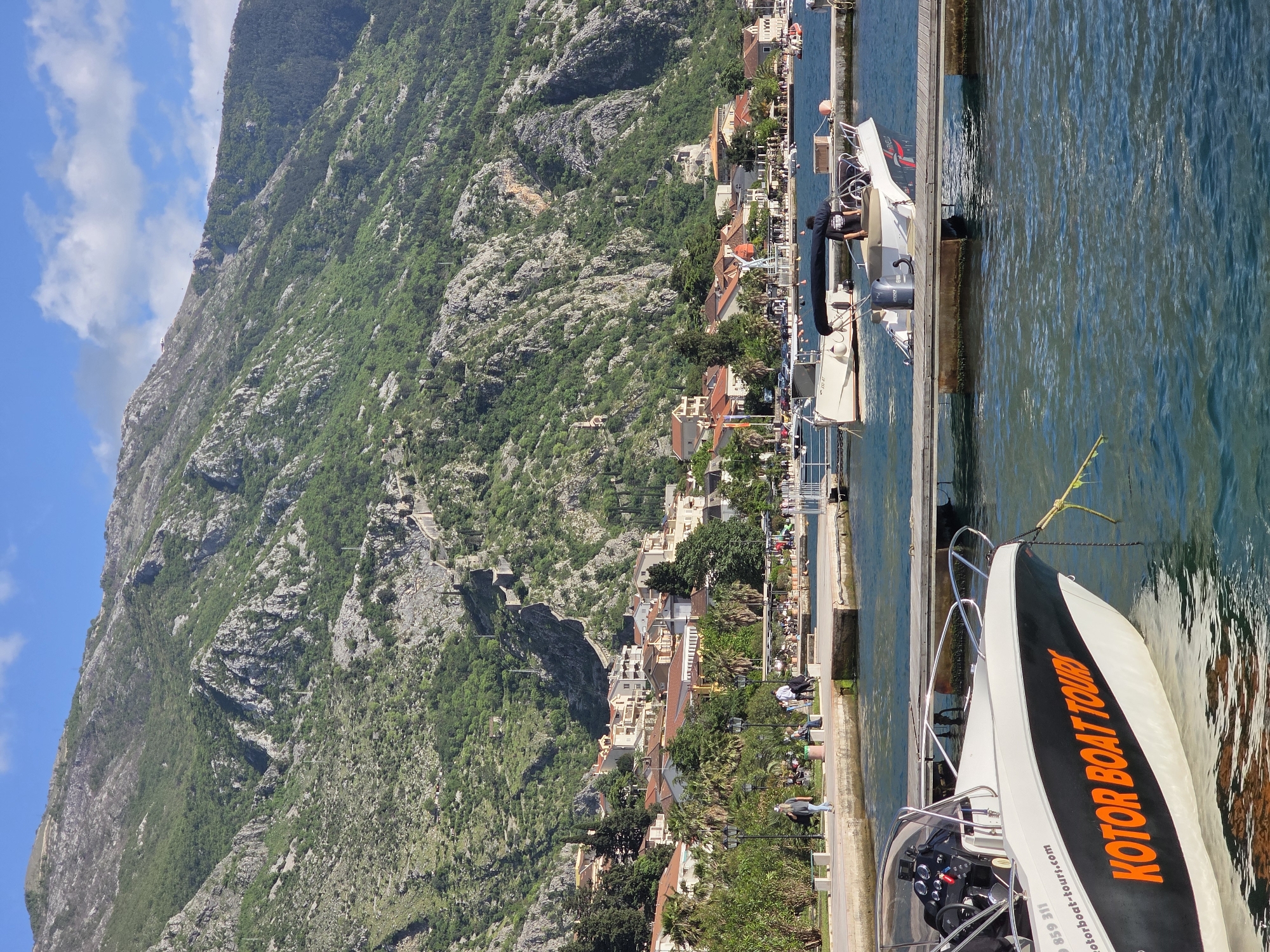 Tourists relax along Dobrota waterfront near historic Kotor walls