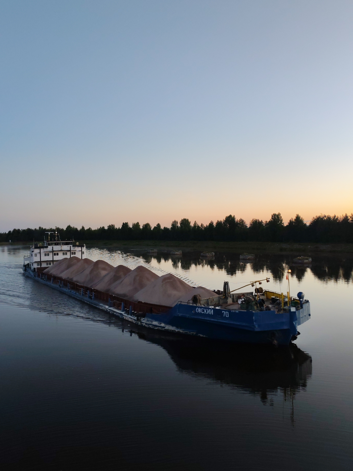 Sand barge drifts down calm river near Devyatiny at dawn