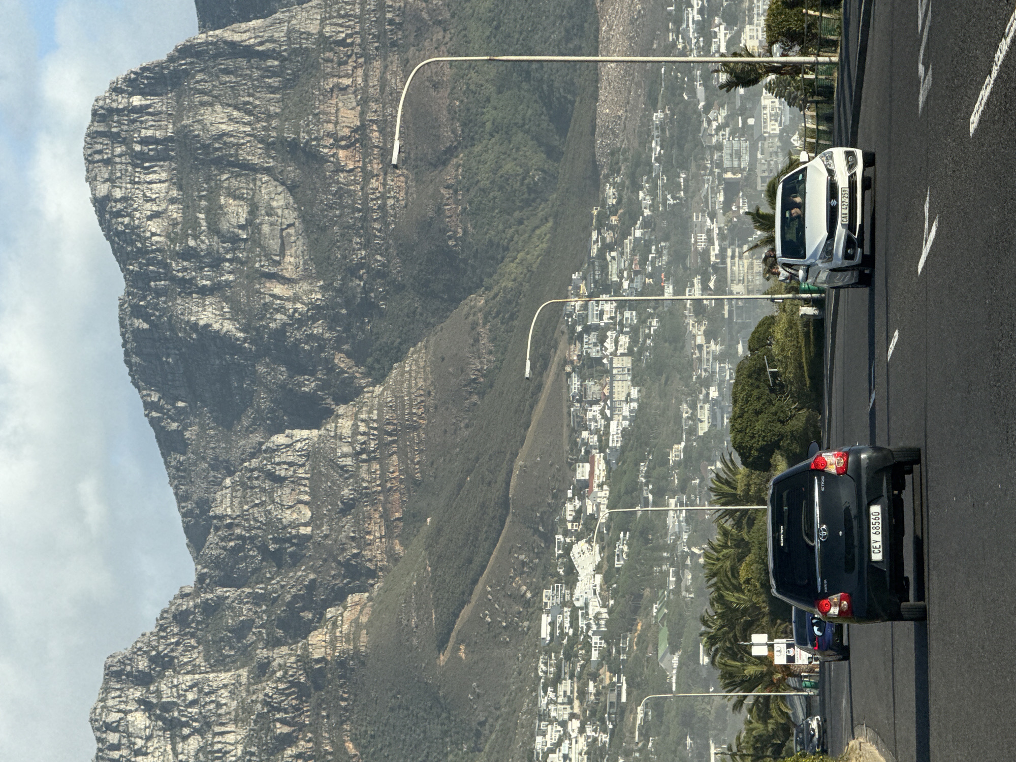 Two cars travel Cape Town road with mountains backdrop