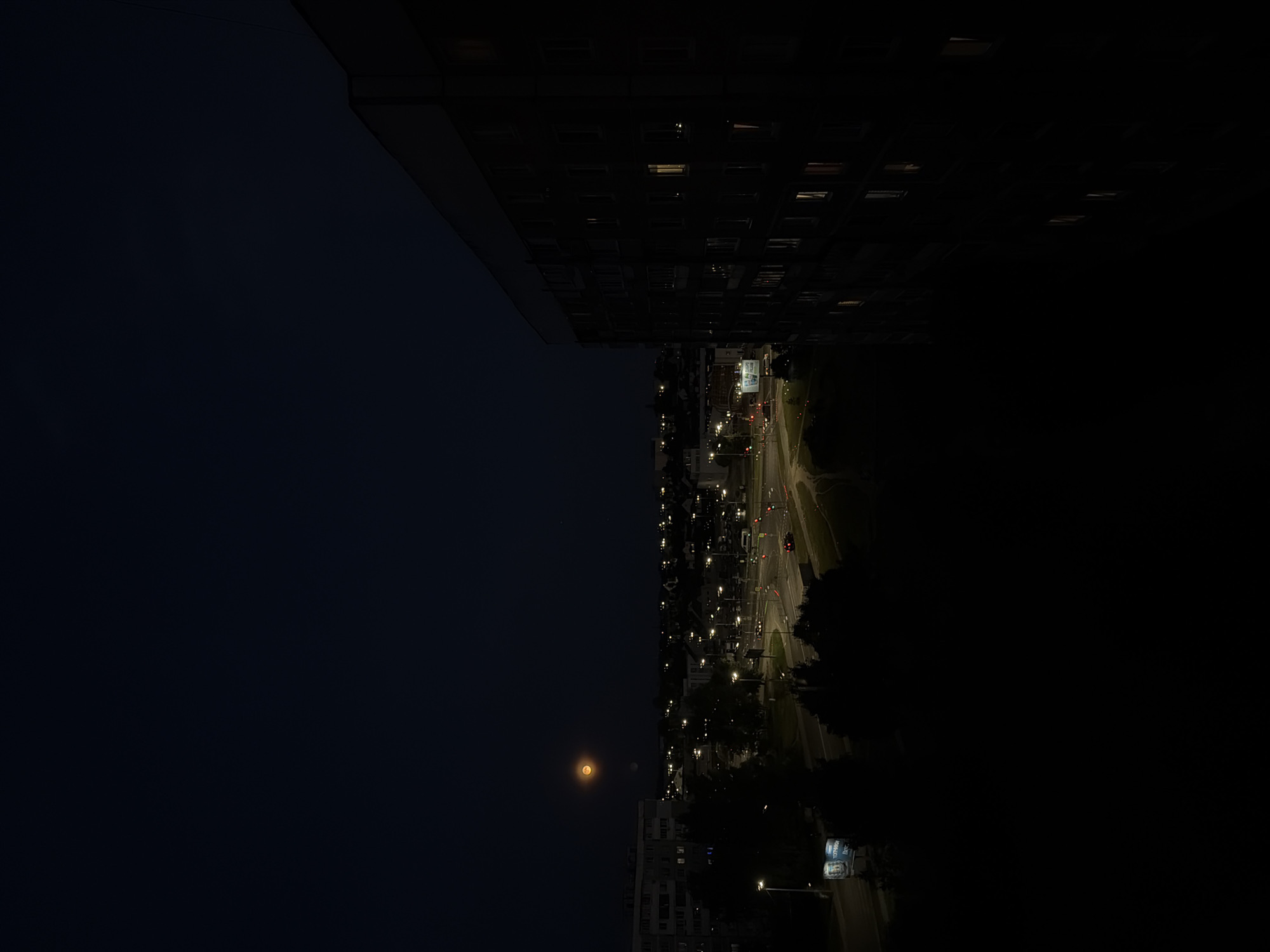 Orange moon rises over Mahilyow residential streets at dusk