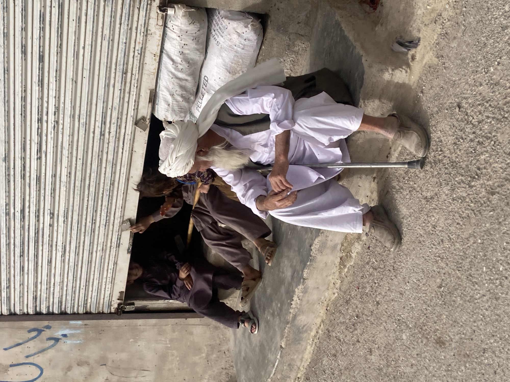 Elderly man in traditional dress sits with walking stick in Quetta