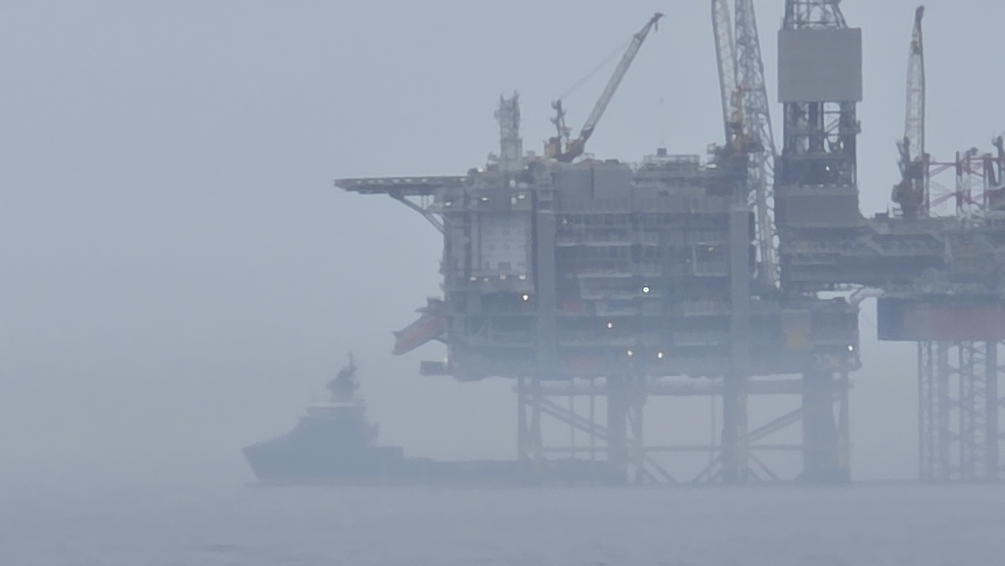 Red vessel operates near oil platform in foggy conditions