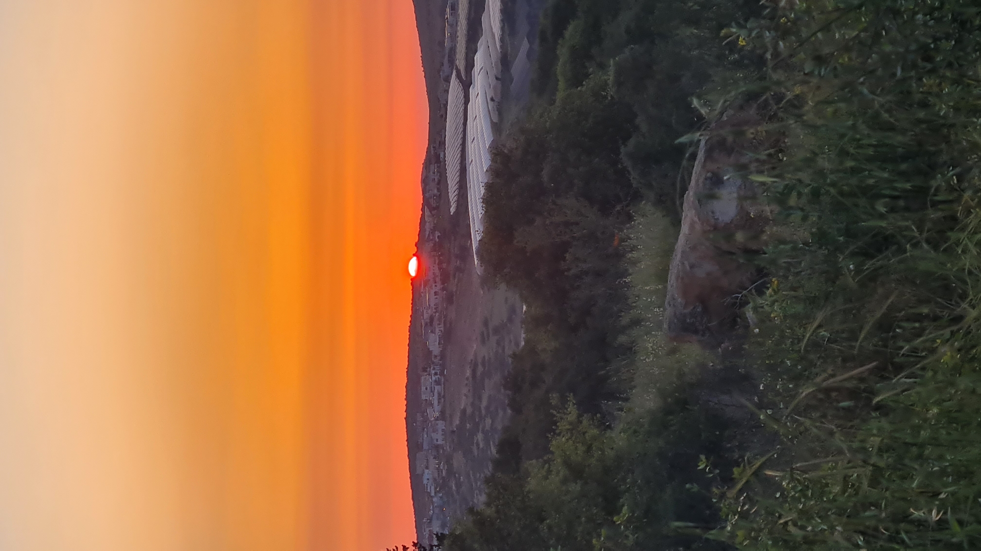 Sunset documented over semi-rural area with wooded terrain