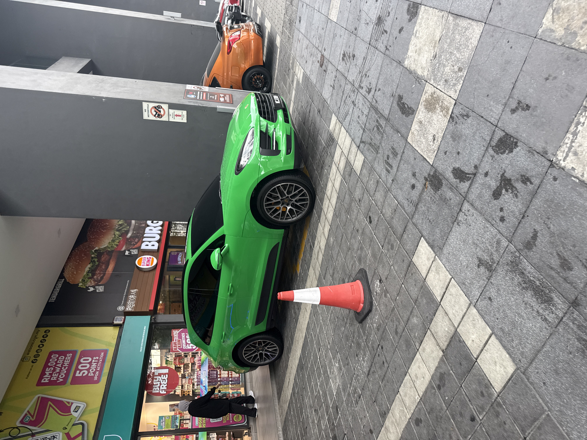 Green Porsche blocks pedestrian walkway near Kuala Lumpur shops