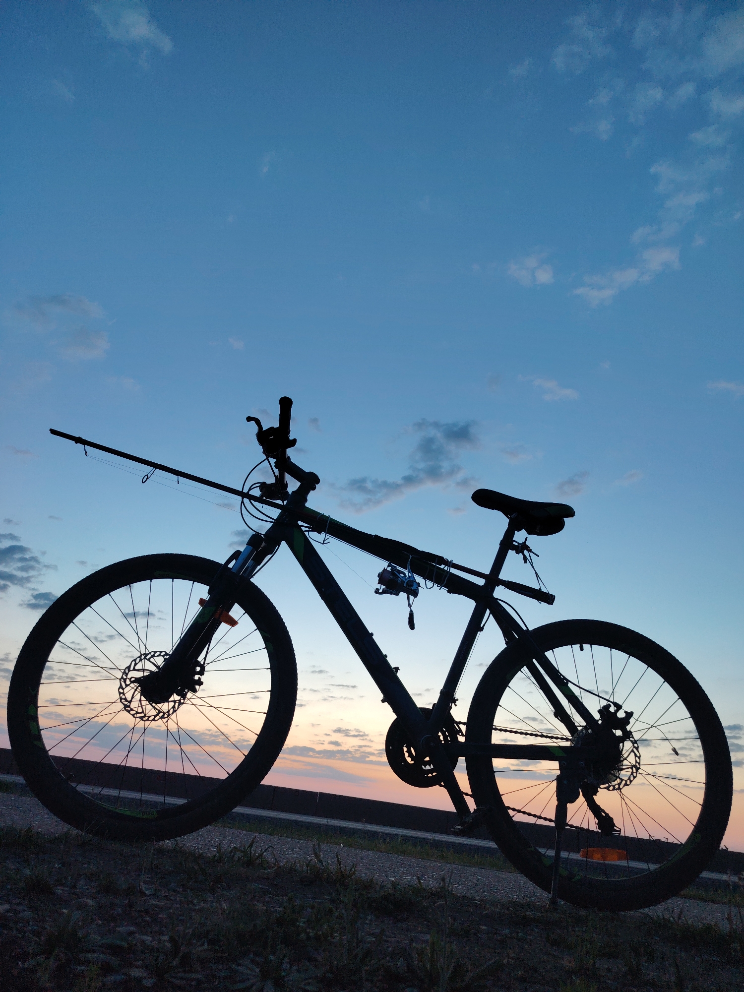 Cyclist with fishing rod travels Chaikovsky streets at dusk