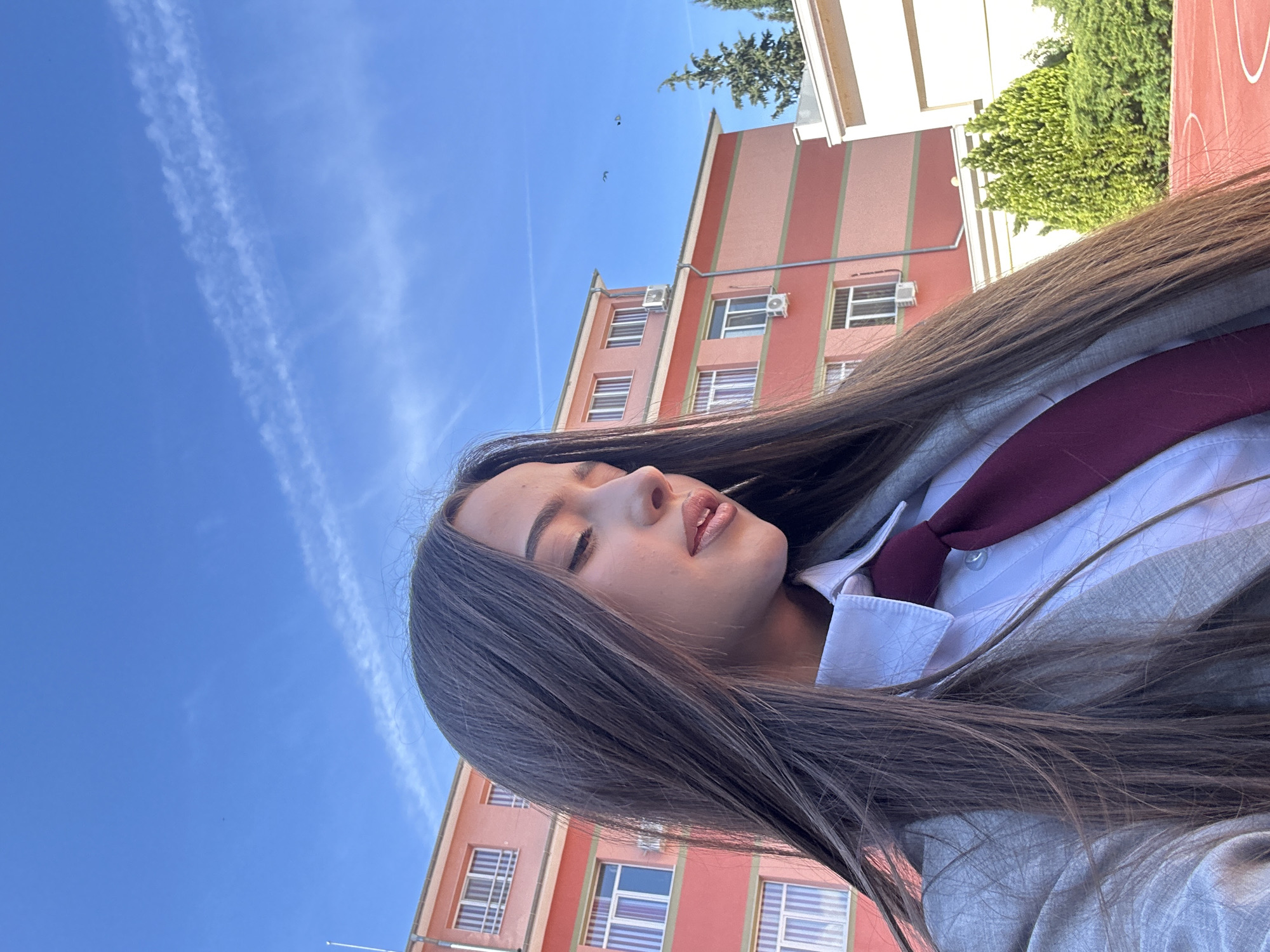 Woman in school uniform poses near reflective surface outdoors