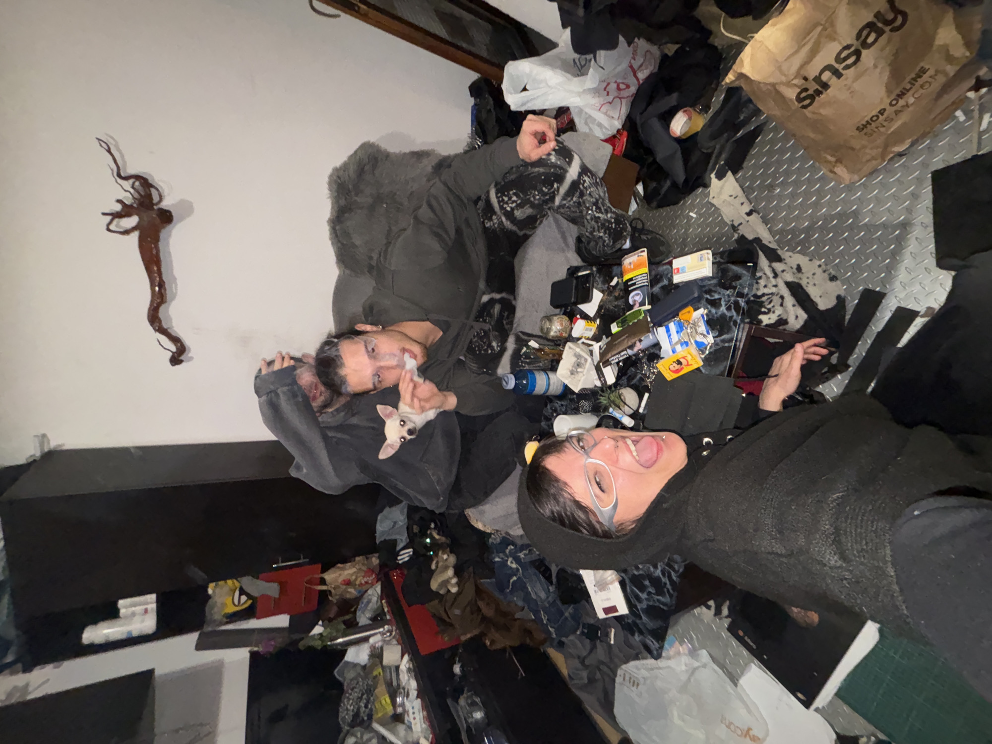 Two people rest on cluttered floor with dog in Sofia