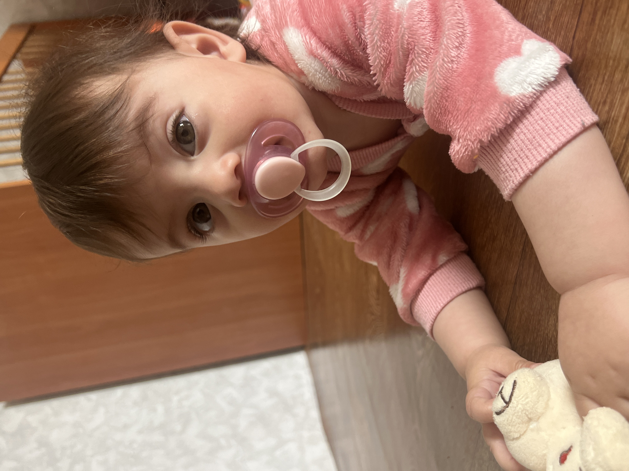 Baby with stuffed toy observed on wooden floor in Elena