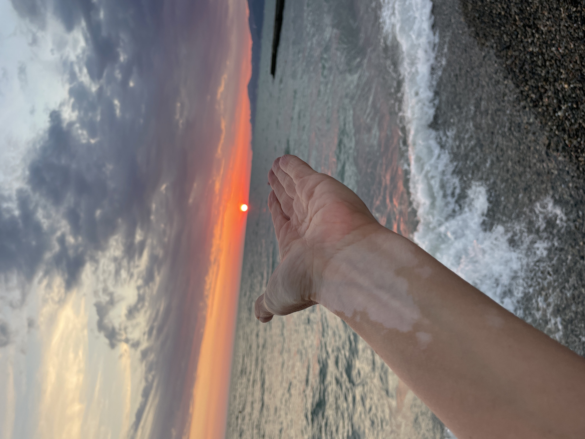 Woman captures sunset selfies on pebbled ocean beach
