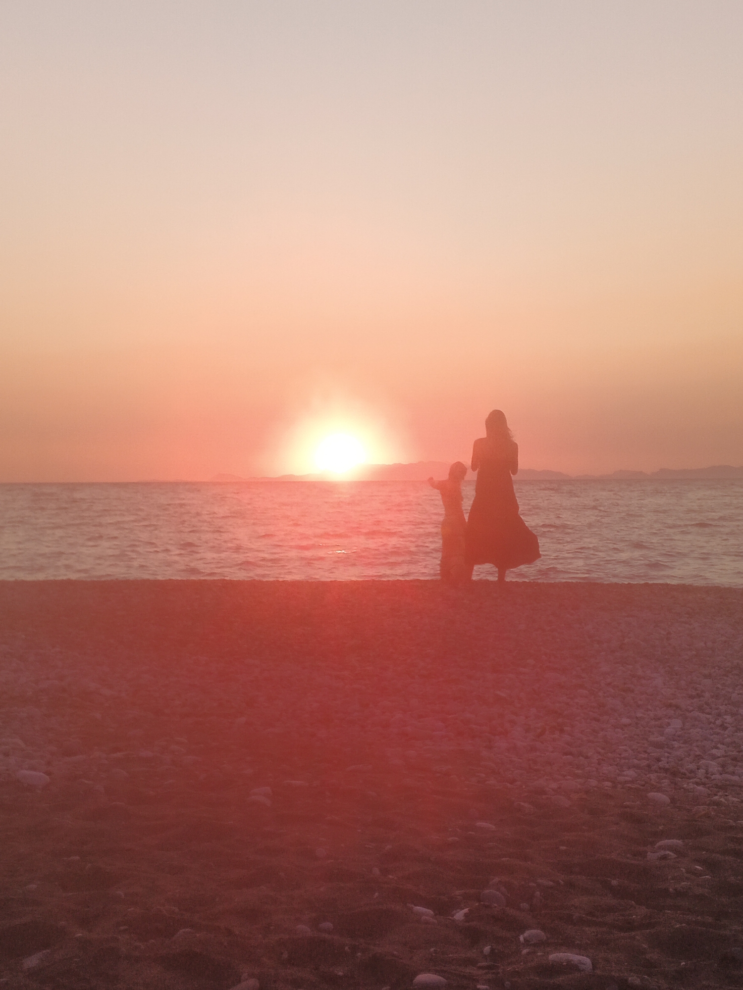 Two silhouettes at the water's edge during a pebble beach sunset
