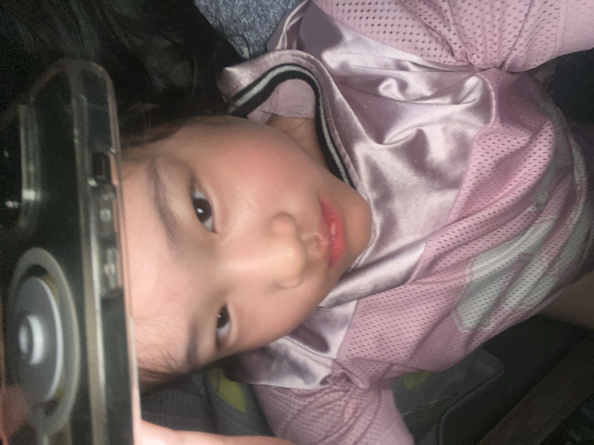 Child with cracked phone rests on bed in pink jersey