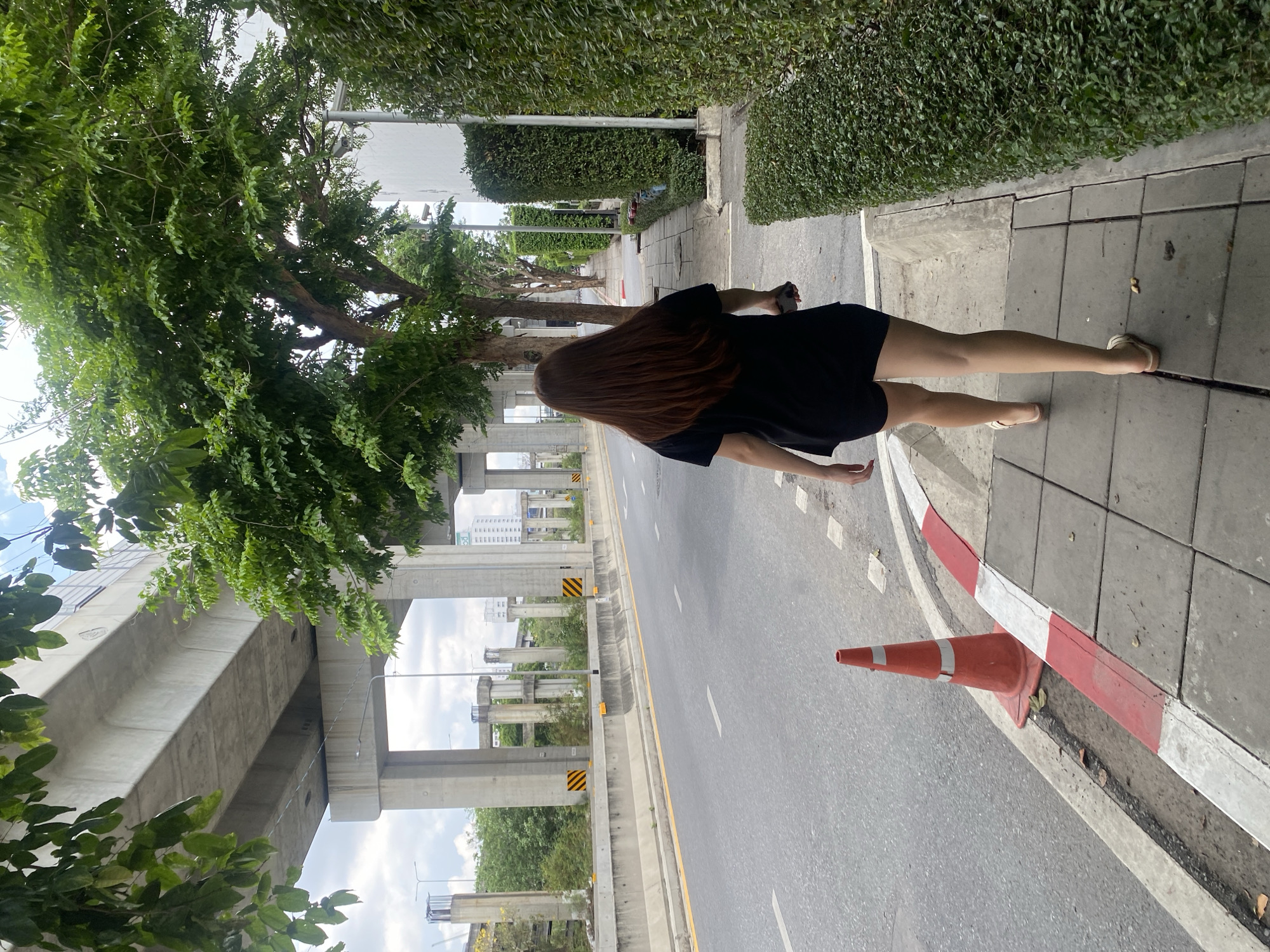 Woman in black dress walks Bangkok sidewalk early morning