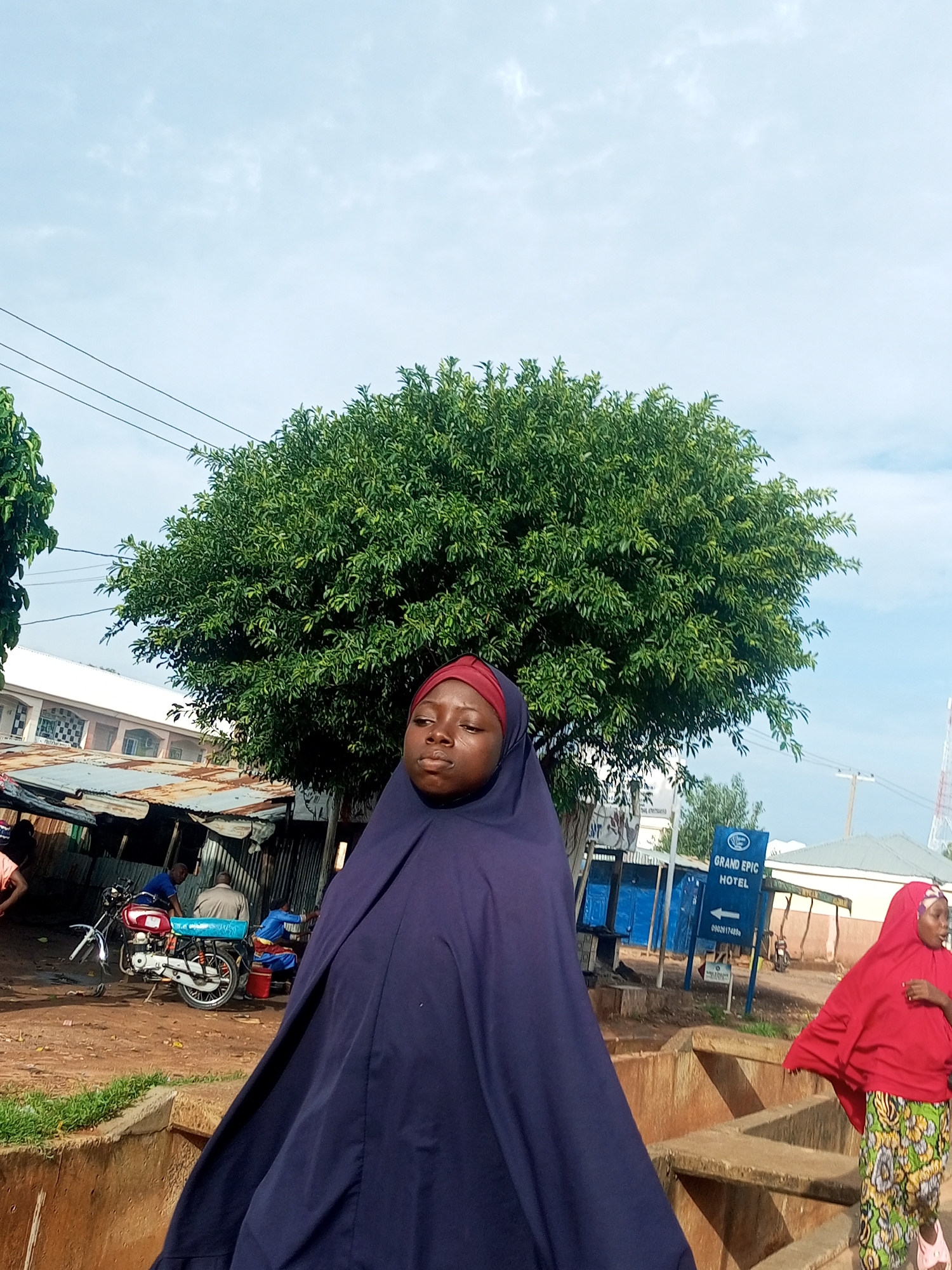 Street scene with lush greenery and a figure in blue hijab