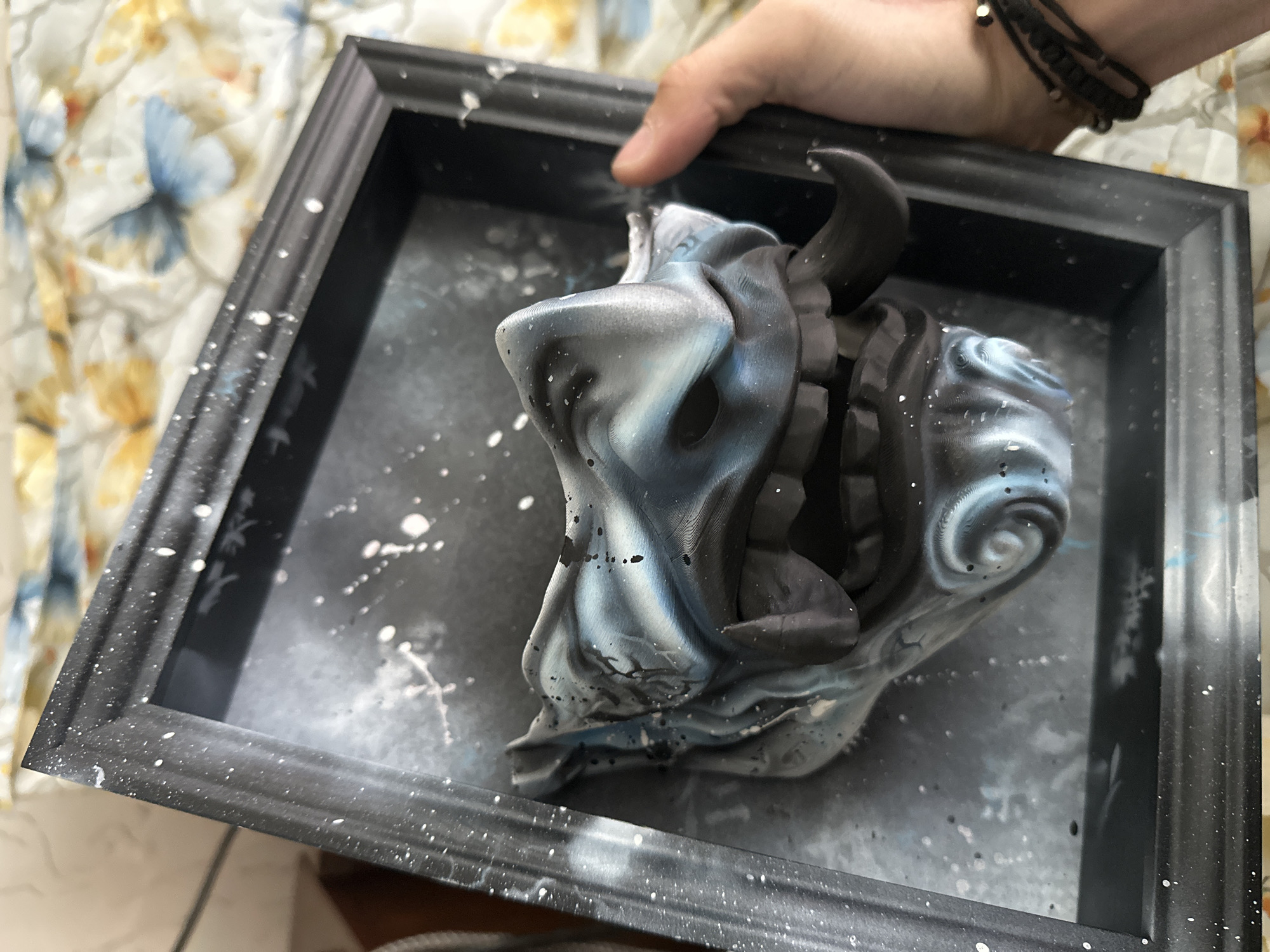 Person displays framed mask artwork with paint splatters in Burgas