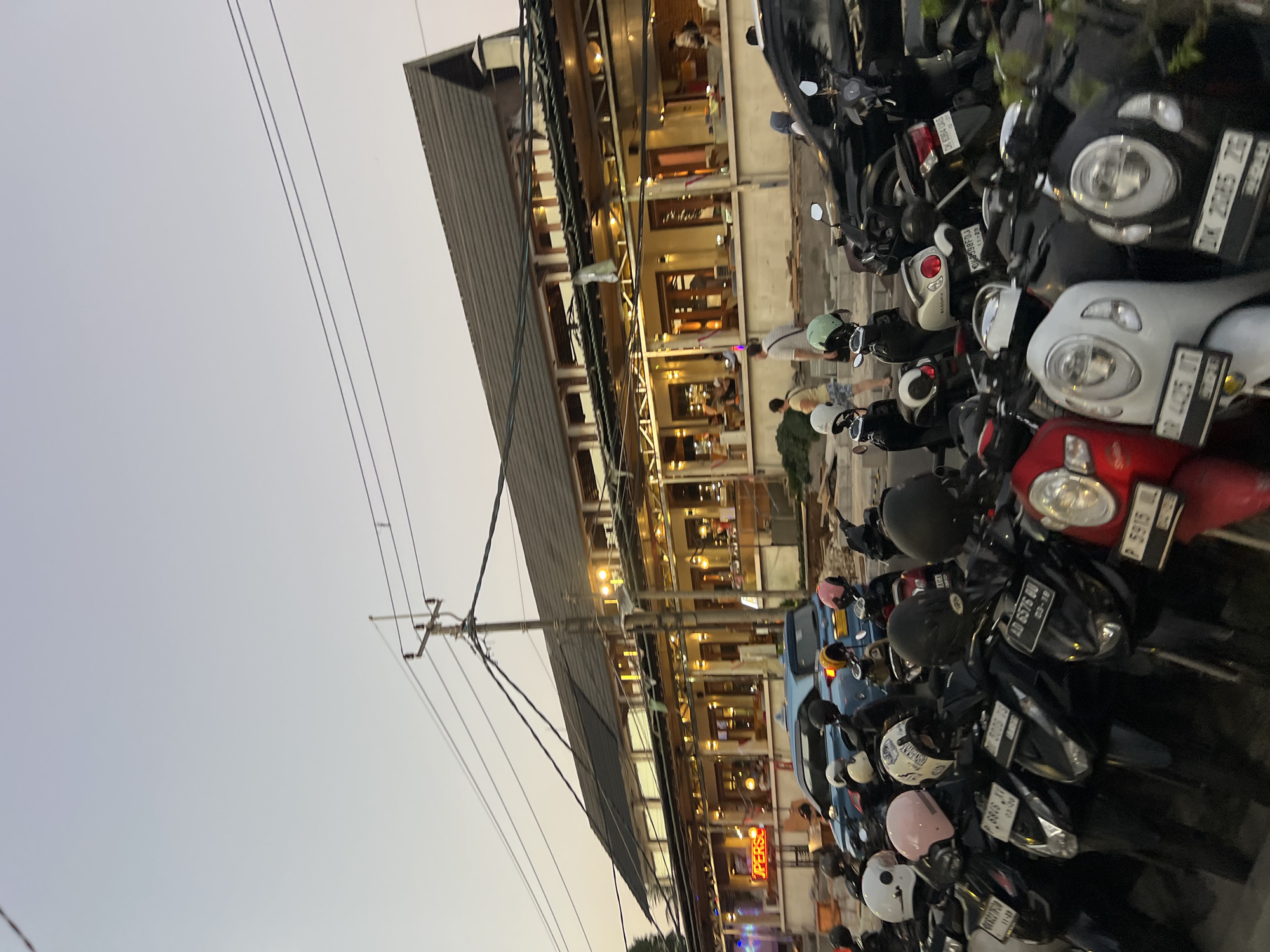 Kuta street at dusk, motorcycles packed outside a lit commercial strip