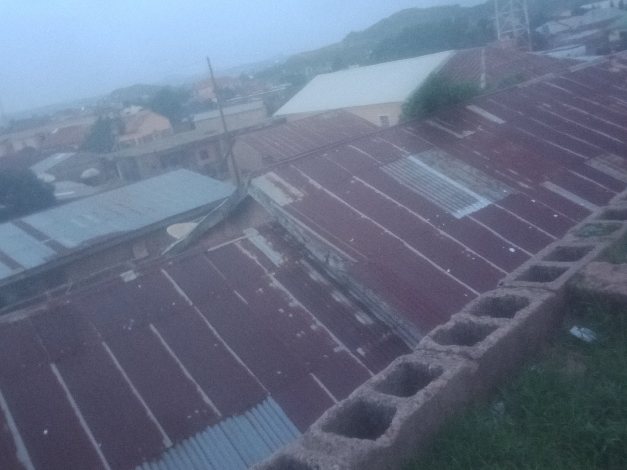 Aerial views show reddish-roofed urban settlement under overcast skies