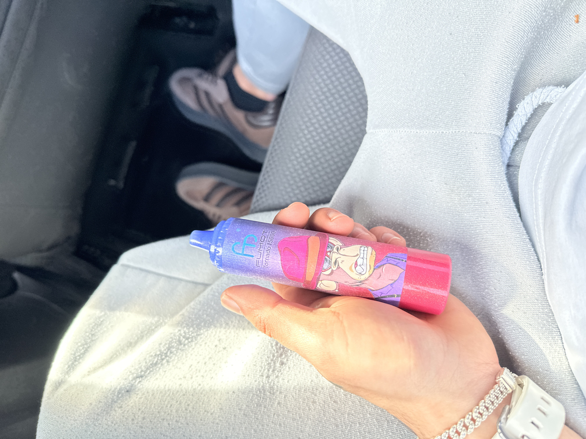 Person holds cartoon-decorated vape device inside vehicle in Zeist