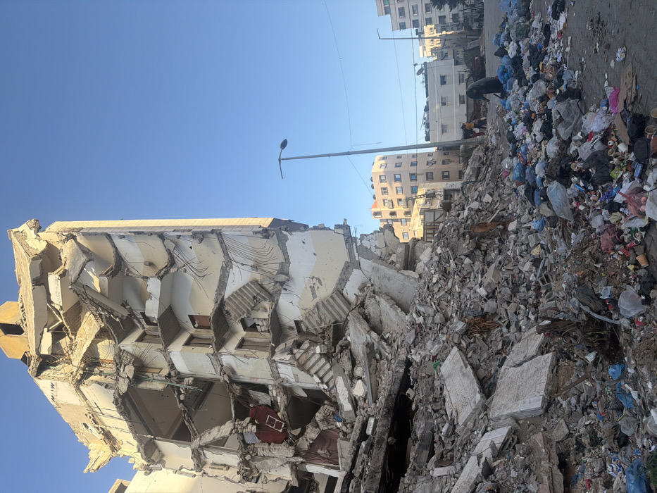 Damaged buildings observed in Gaza with pedestrians, debris visible