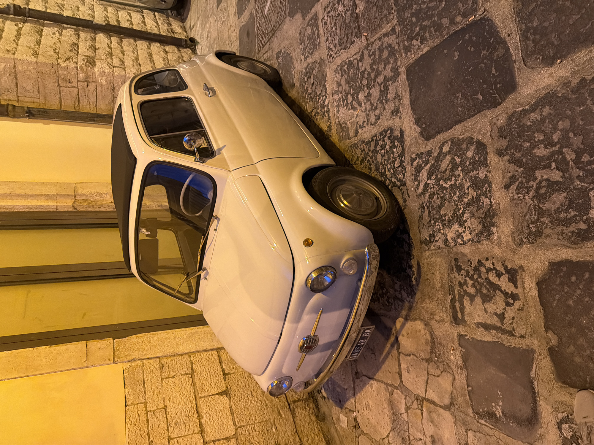 Pale yellow Fiat 500 parked on Bari's cobblestone streets
