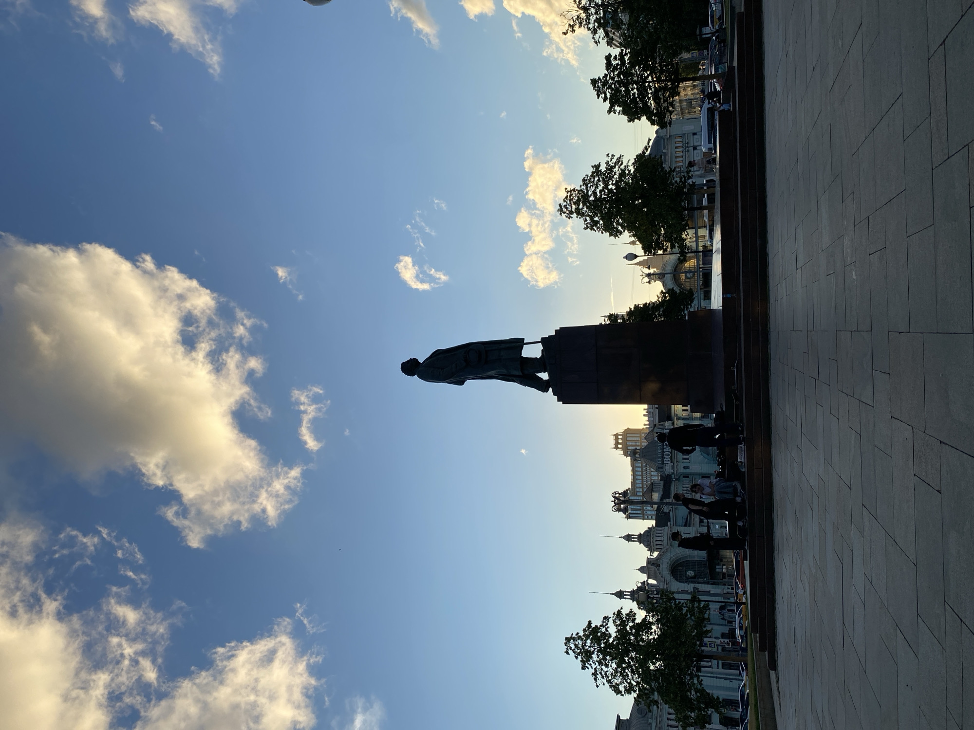 City plaza at dusk: statue, golden light, and a street scene