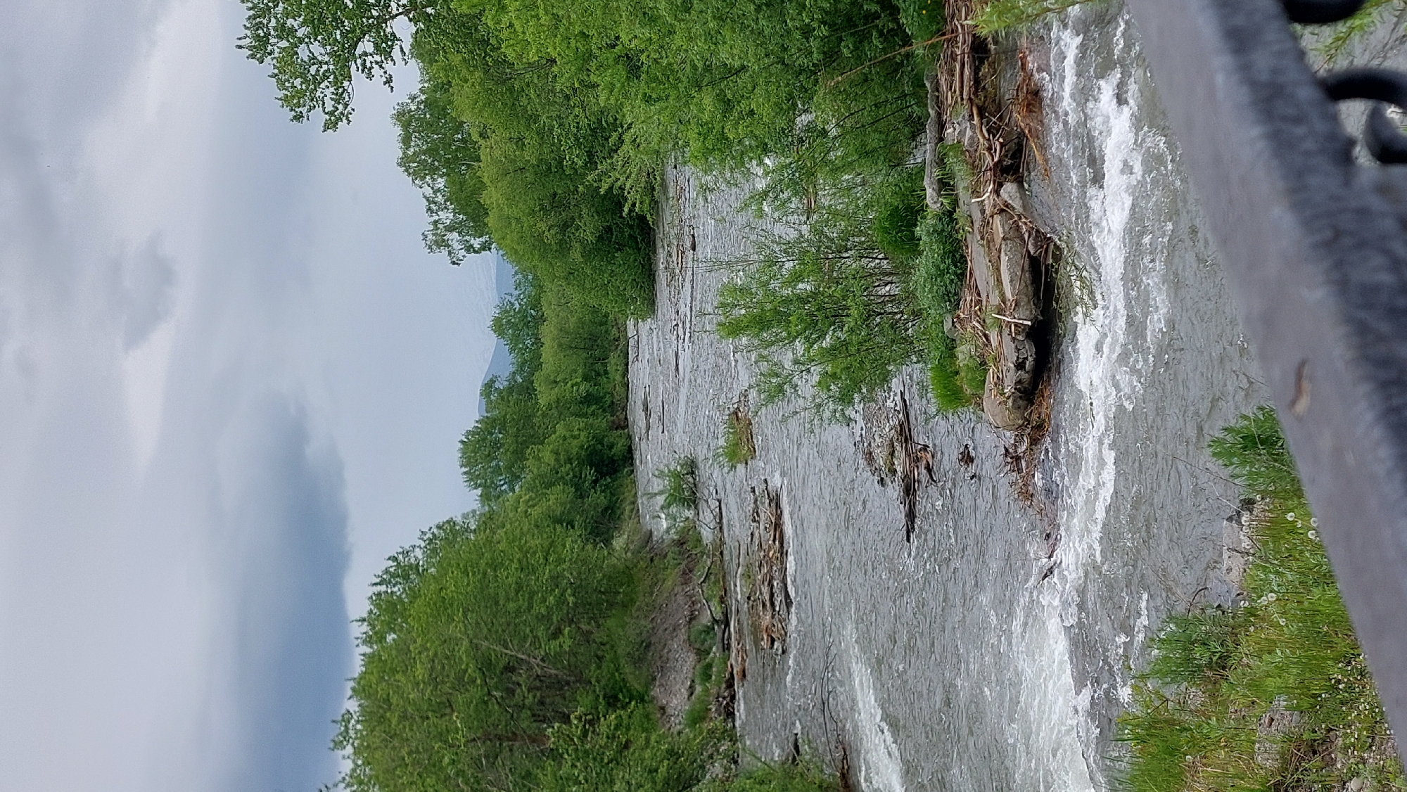 Debris-filled river runs fast through Koryaki under cloudy skies