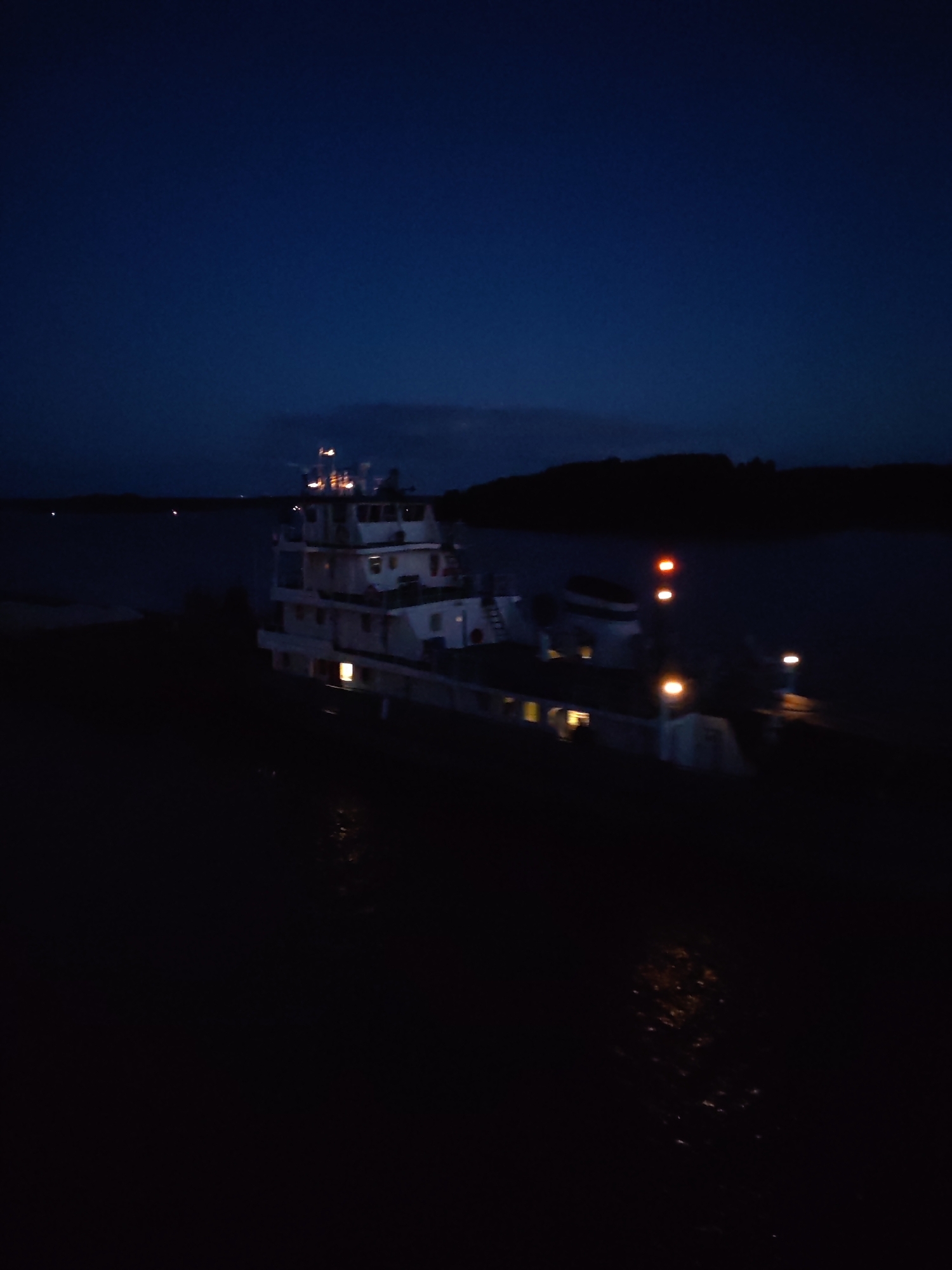 Tugboat pushes barge upriver at night near Нова, Russia