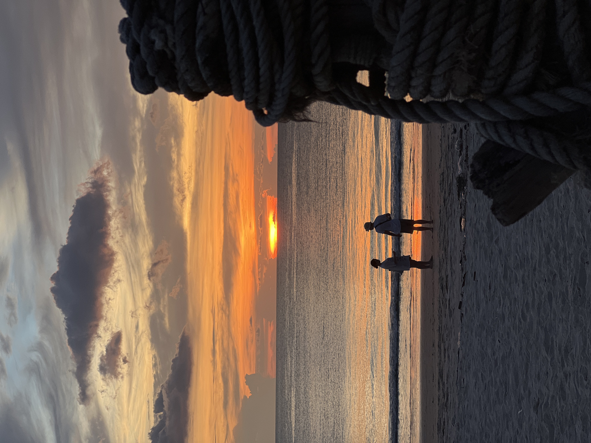 Two people witness sunset on beach, silhouettes against golden sky