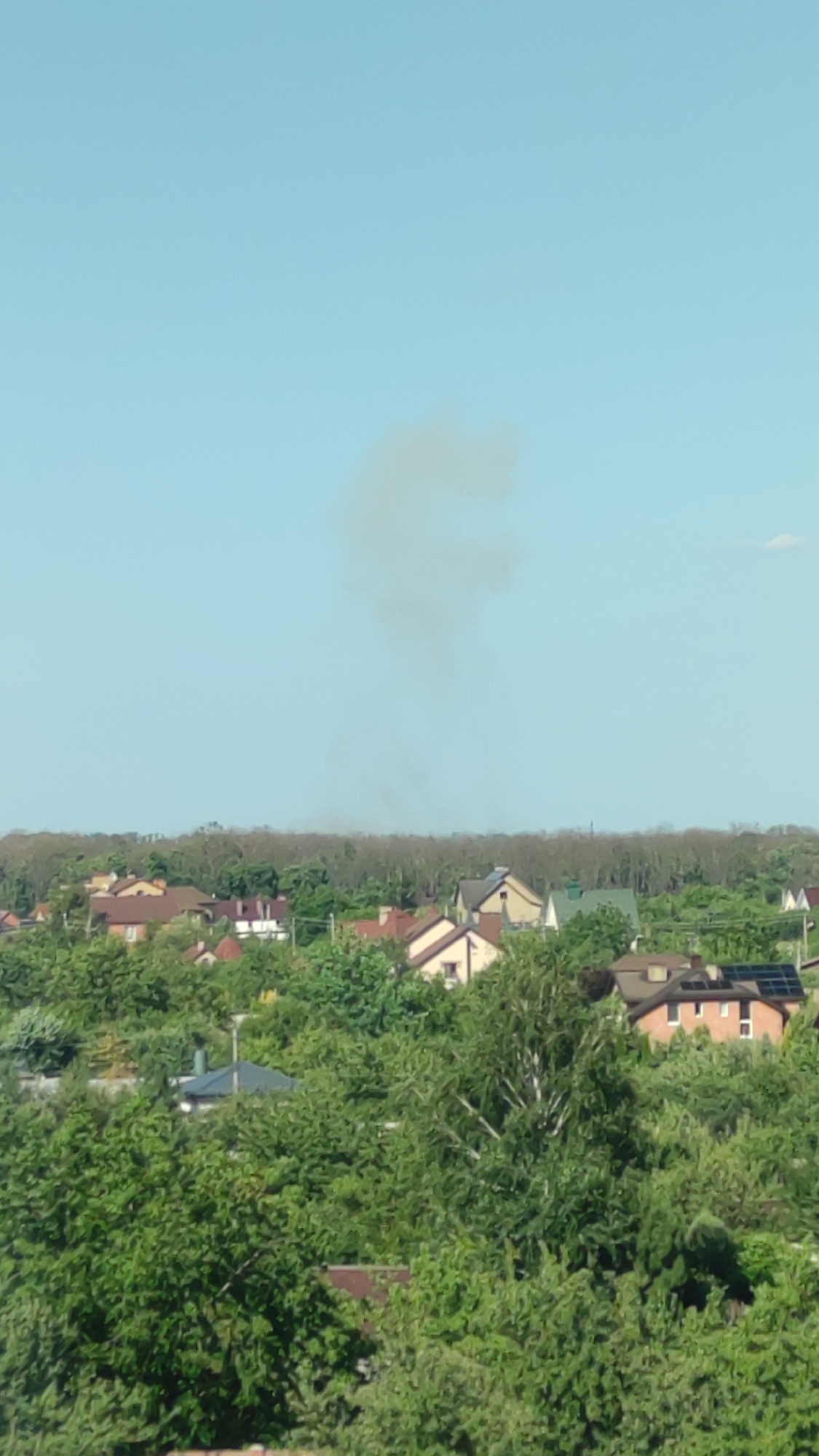 Dark smoke rises over suburban neighborhood on clear afternoon