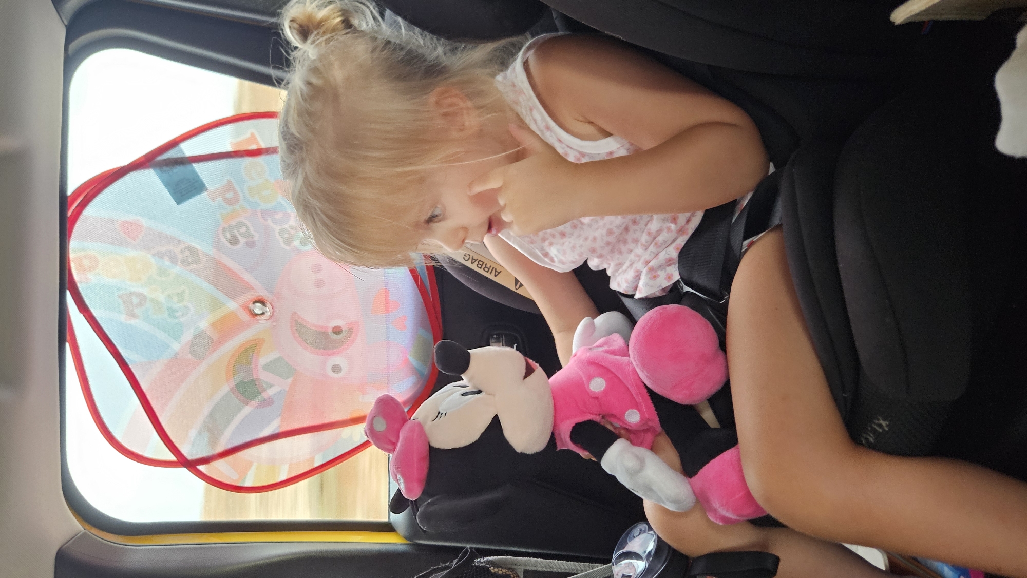 Minnie Mouse plush in hand, pointing from a car seat in Spain