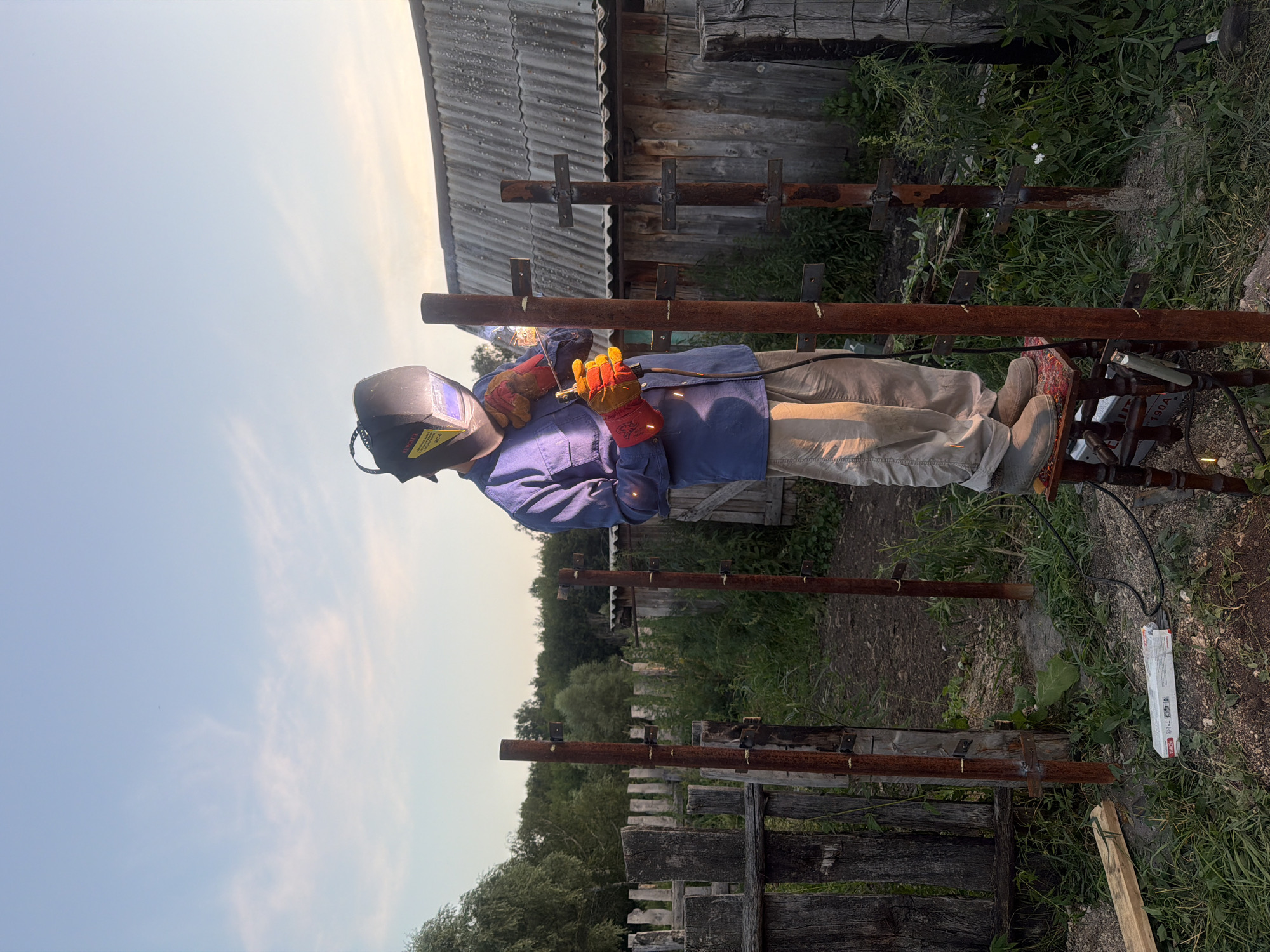 Welding metal posts at dusk in a Kuseevo village yard