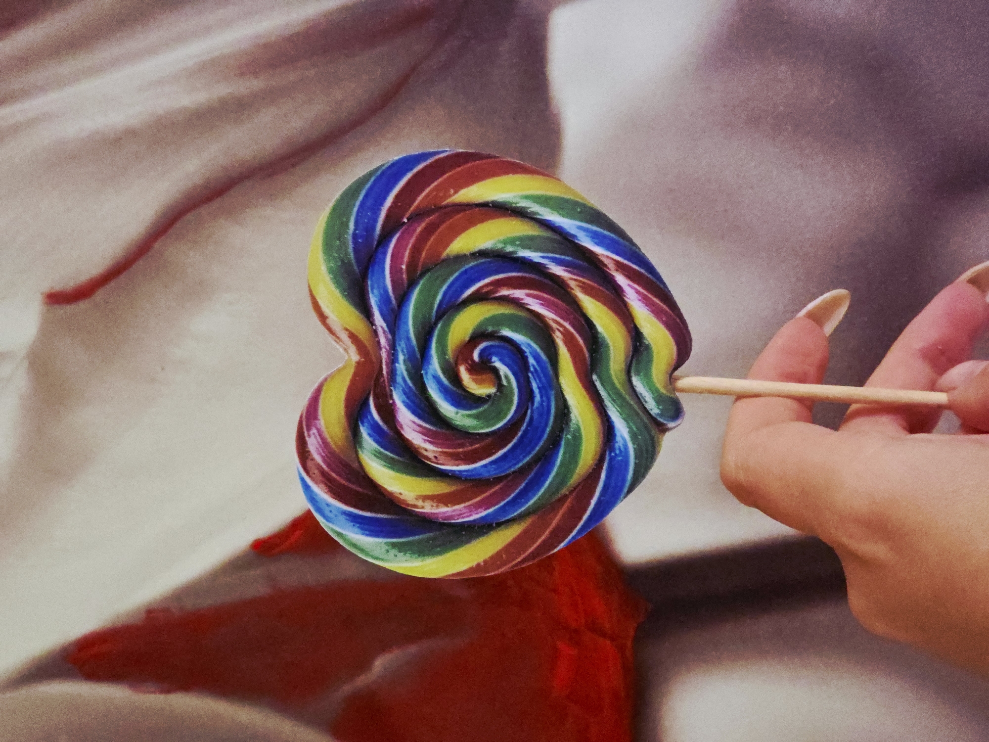 Heart-shaped rainbow lollipop photographed in garden settings