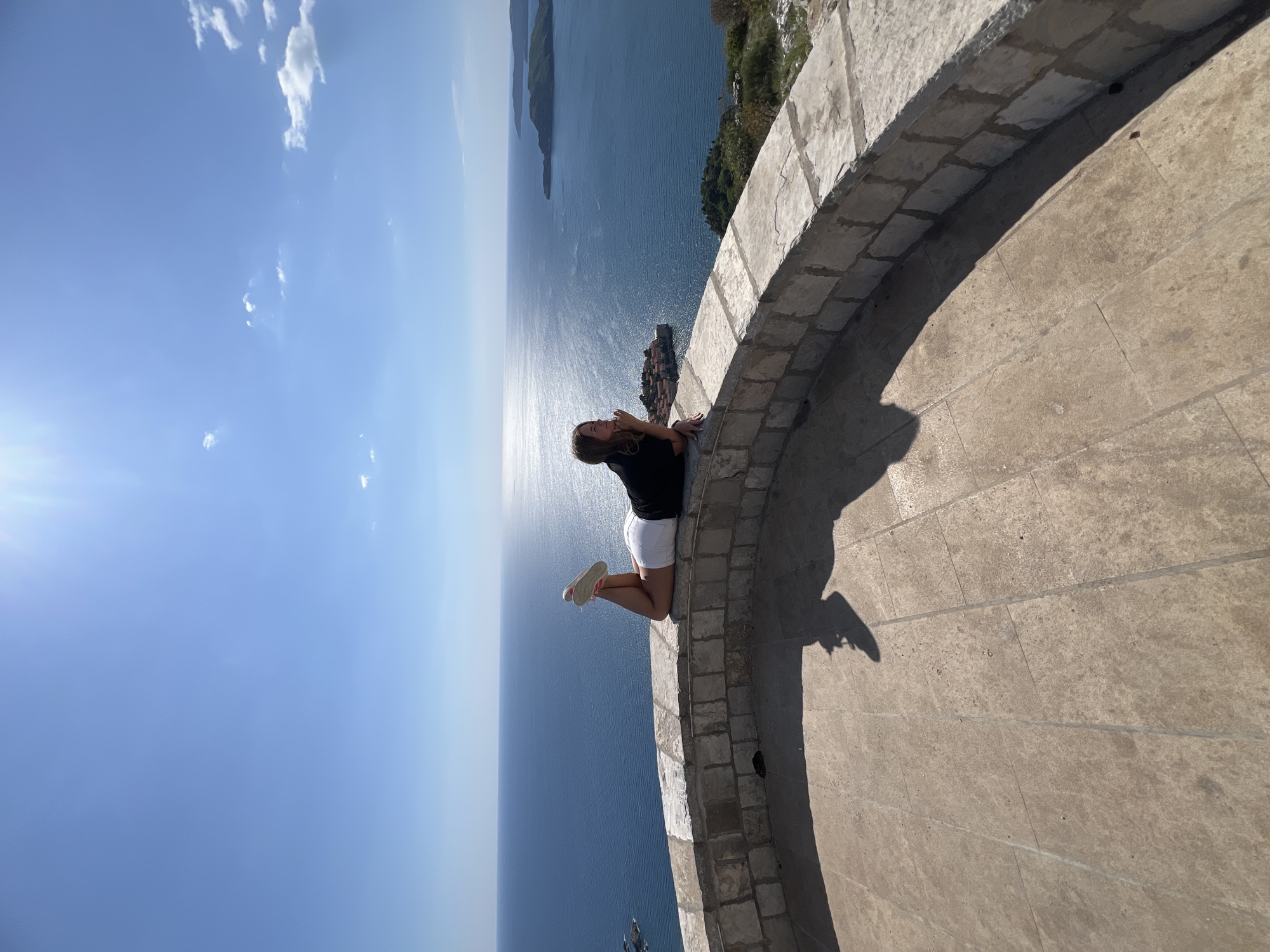 Woman rests on stone wall overlooking Adriatic at Sveti Stefan
