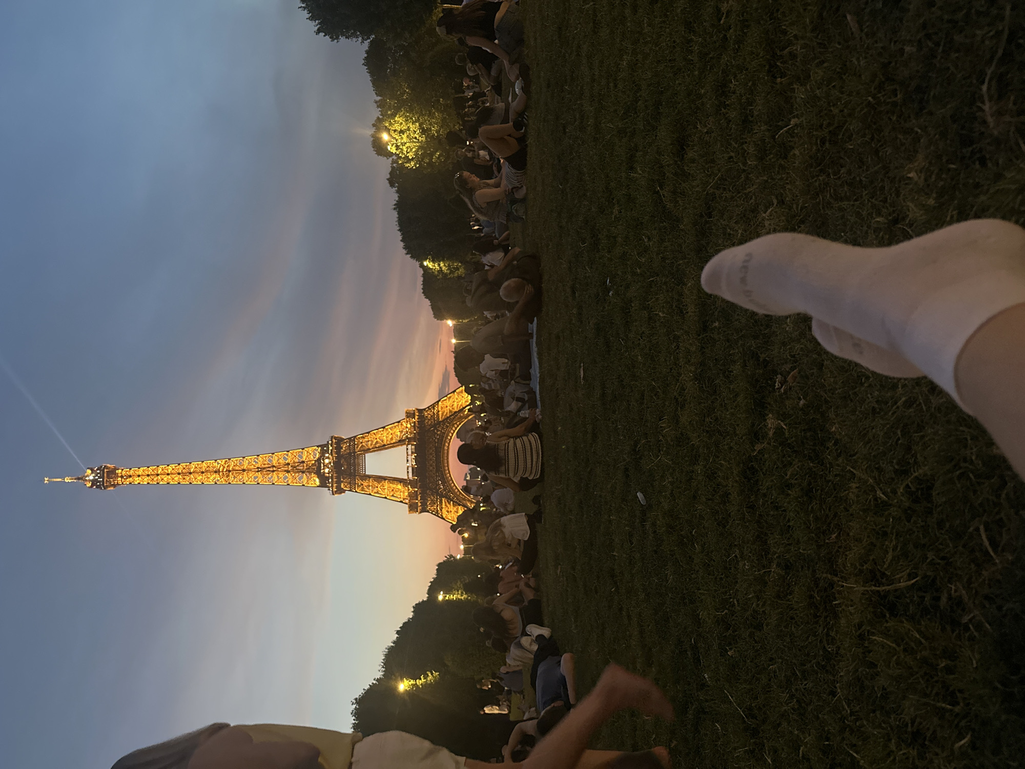 Eiffel Tower glows at dusk over a relaxed Champ de Mars crowd.