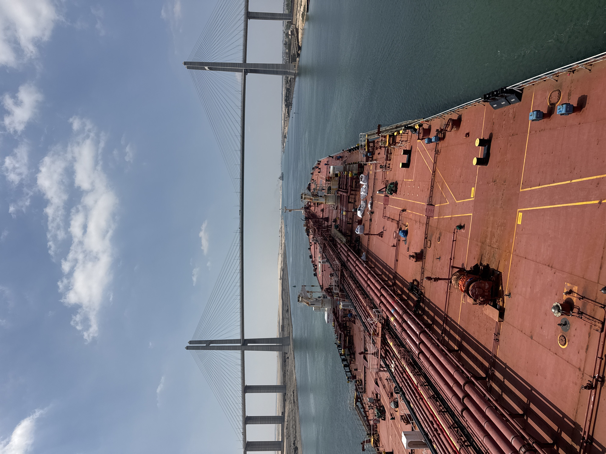 Red cargo ship transits the Suez Canal beneath a cable-stayed bridge