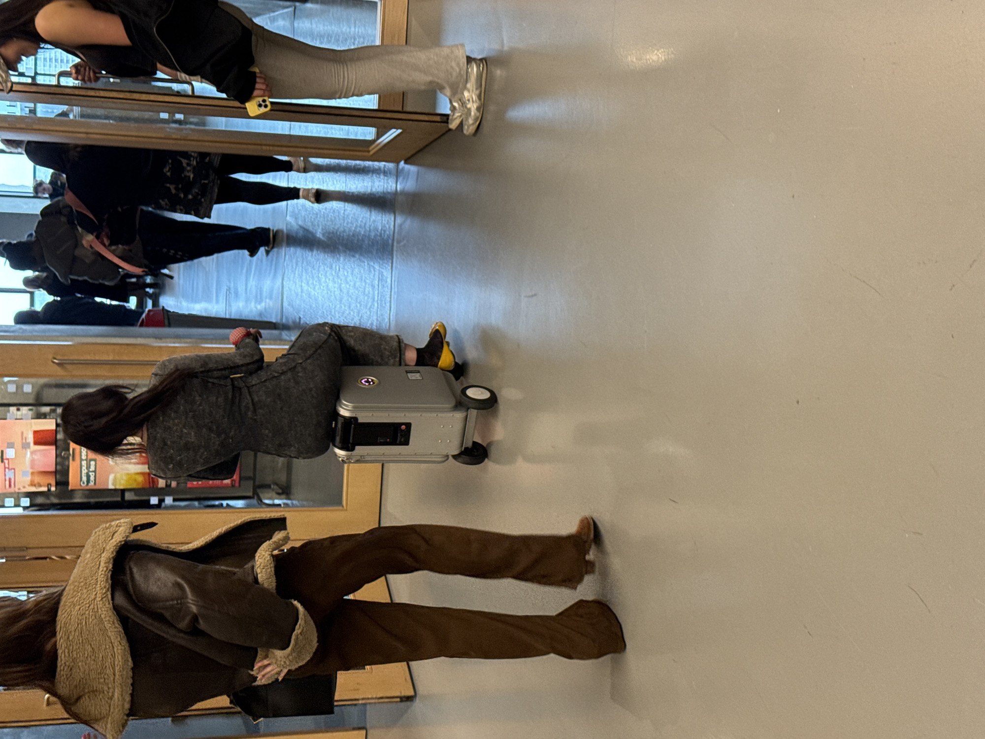 Travelers navigate London building entrance with wheeled luggage