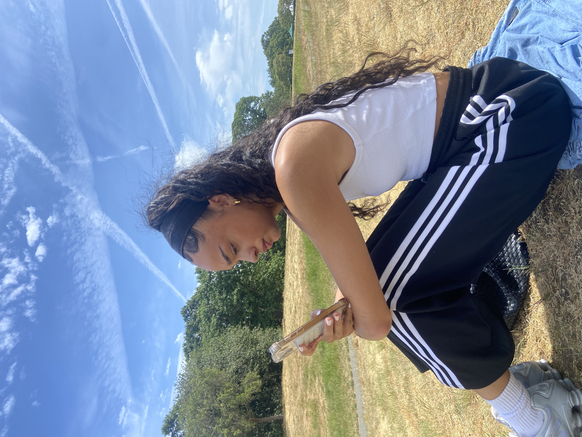 Woman crouches in London park examining ground on sunny day