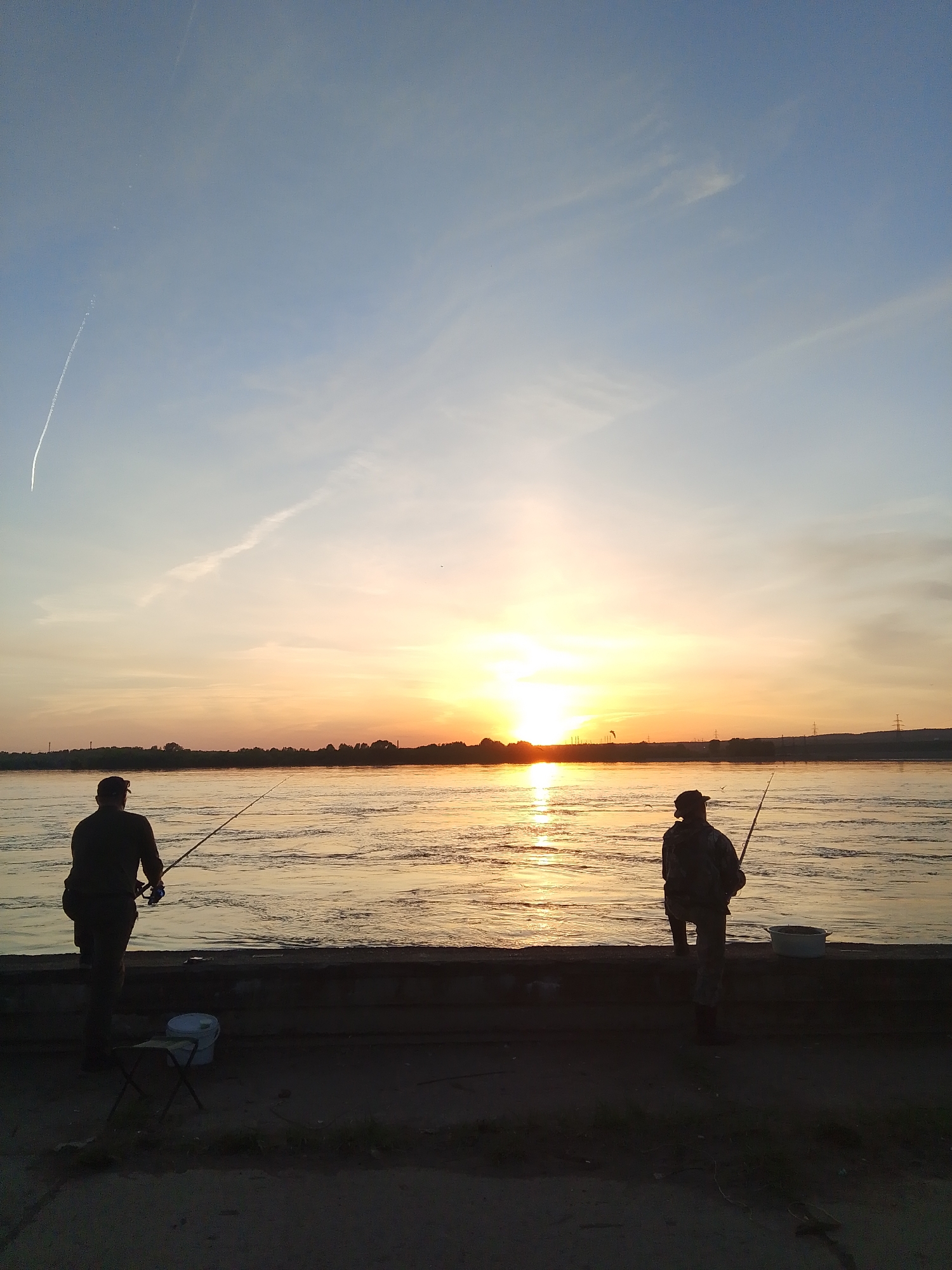 Two anglers fish at sunset on Chaikovsky river embankment