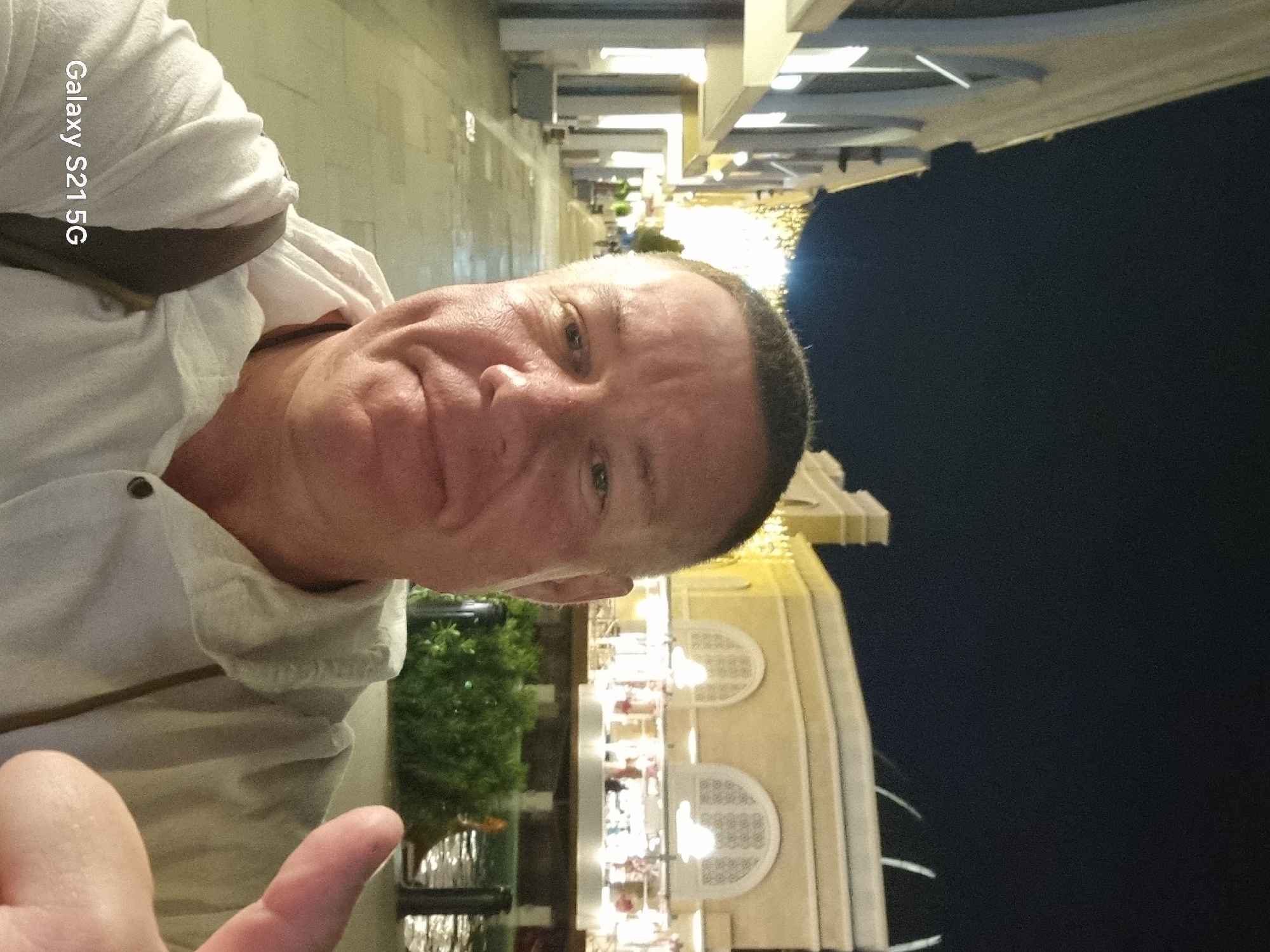 Man poses for nighttime selfie outside illuminated building in Serik