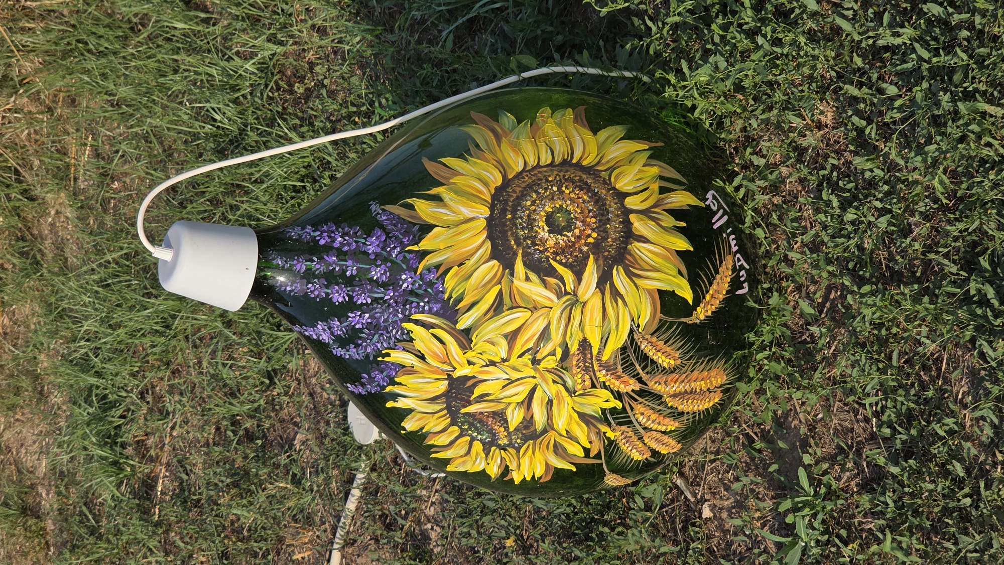 Painted demijohn repurposed as a light, sitting on grass in Tuscania