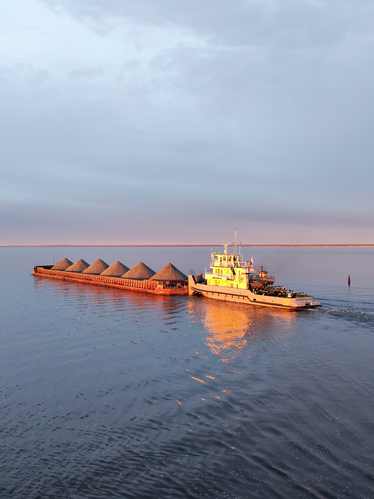 Tugboat pushes gravel-laden barge through Russian waterway
